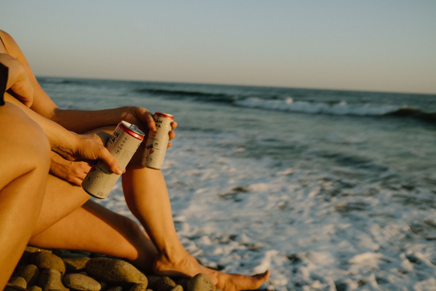 Legs of beachgoer relaxing by the ocean waves during golden hour.