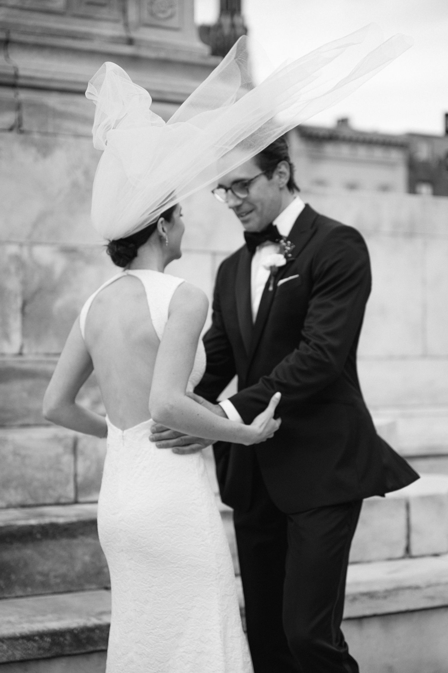 Elegant black and white wedding photo of couple in formal attire on stone steps.