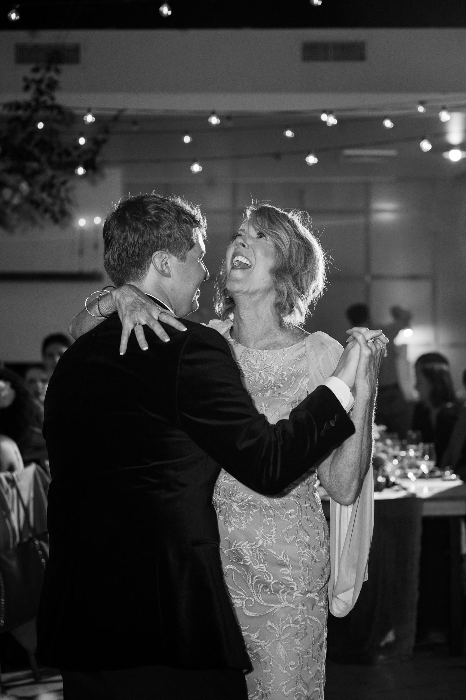 A candid black and white photo of a couple sharing their first dance at a wedding reception.