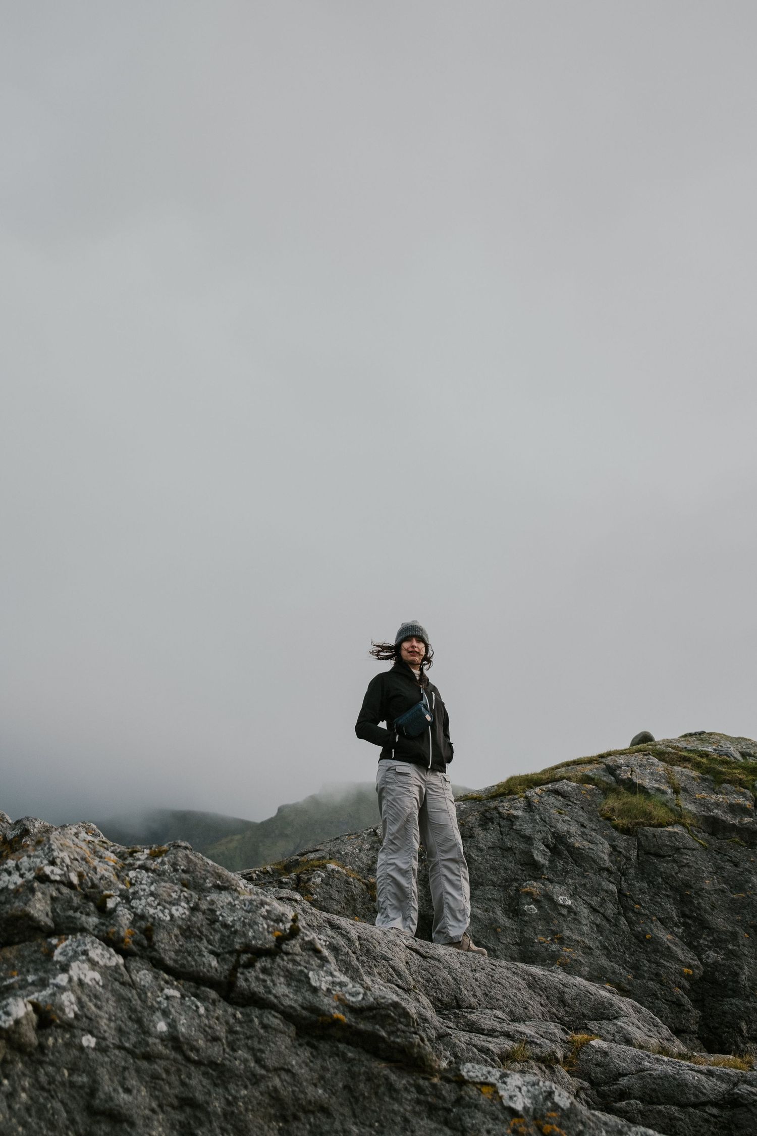 Silhouetted figure stands on rocky cliff edge against moody gray sky.