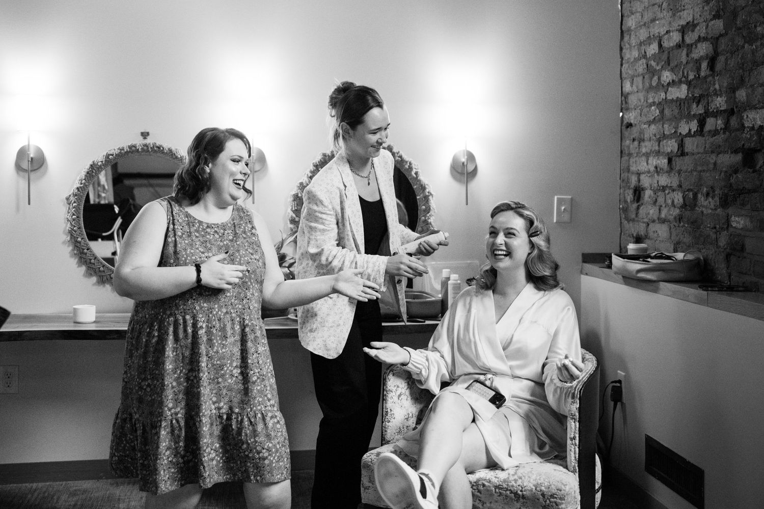 Wedding party members share joyful moments while getting ready in a stylishly lit dressing room.