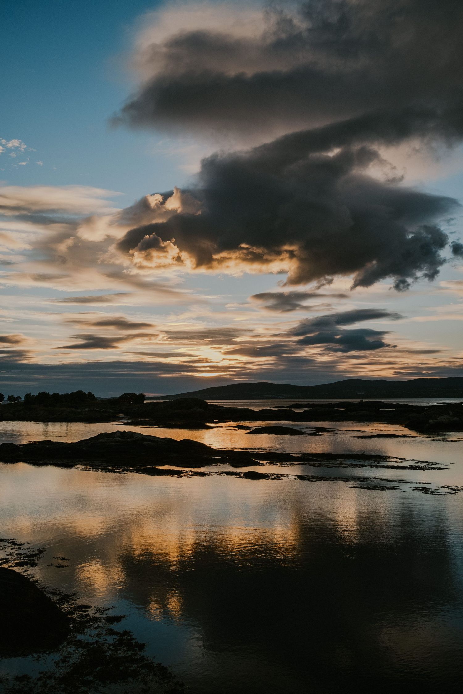 Dramatic sunset sky with dark clouds reflecting in calm coastal waters.