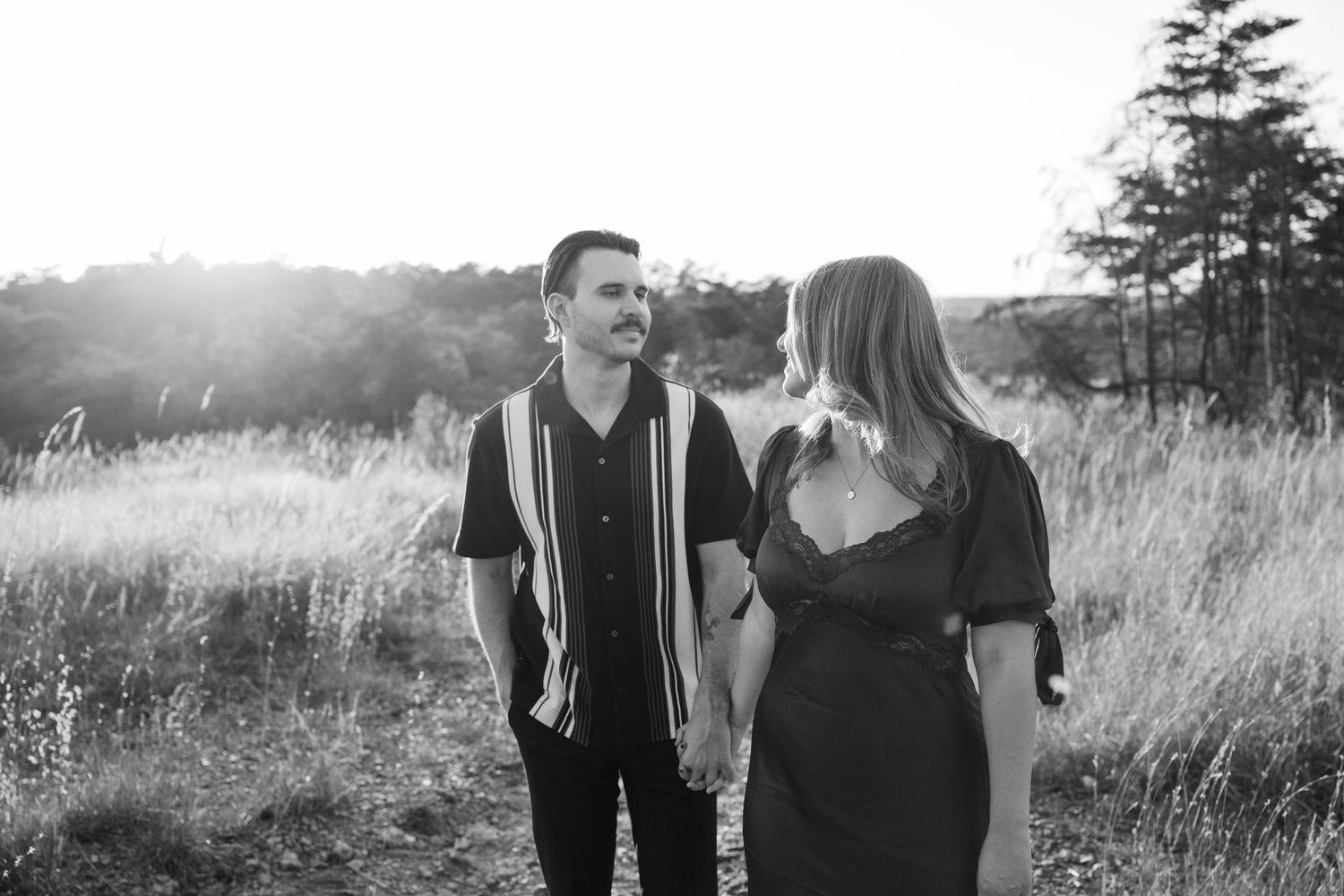 A couple sharing a romantic moment in a field of tall grass during sunset in black and white photography.