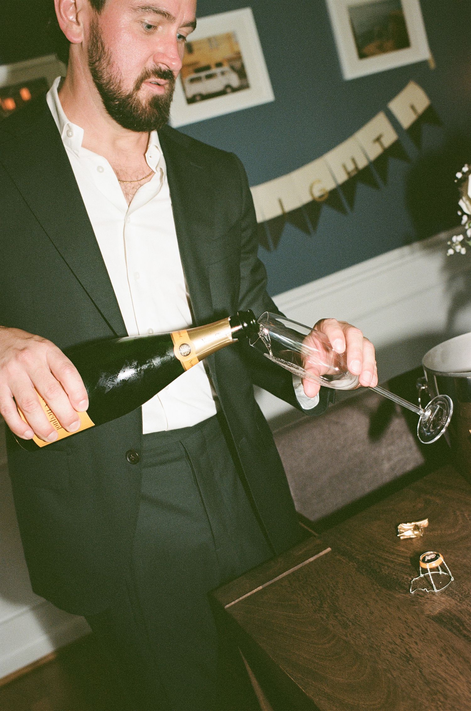 Series of shots showing hands opening a champagne bottle and pouring into glasses on a dark wooden table.