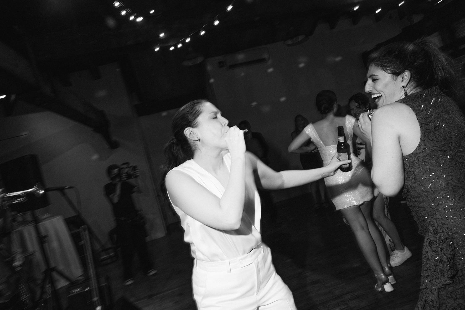 Two figures dancing energetically at a party with twinkling lights in the background.