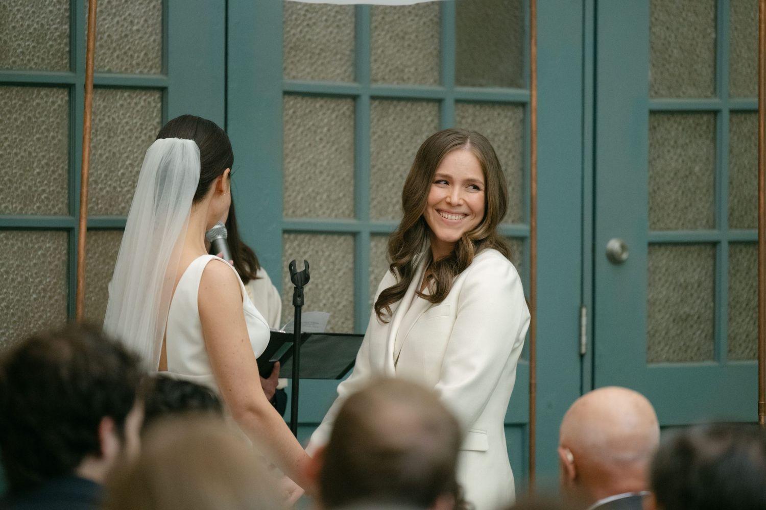 An indoor wedding ceremony with teal paneled windows in the background.