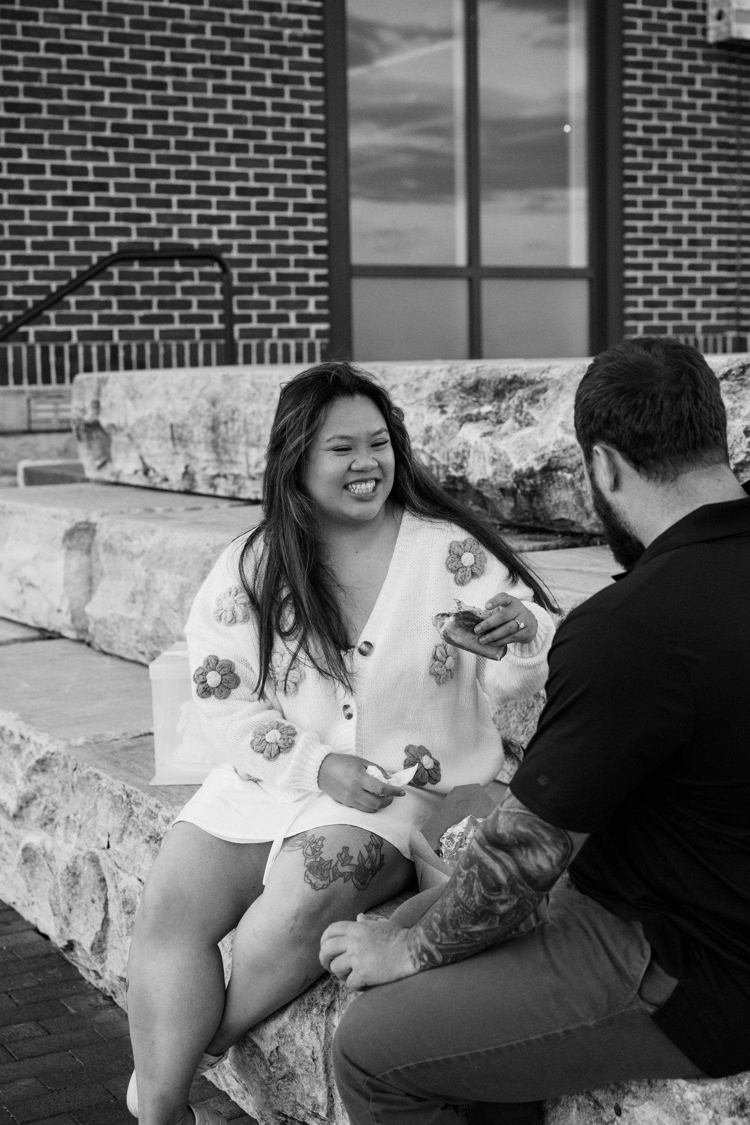 A couple shares a tender moment together on a brick patio during an engagement photoshoot in black and white.
