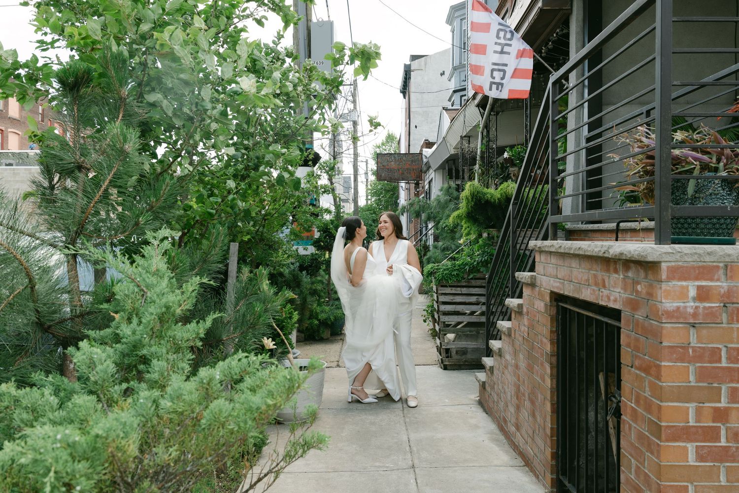 White-clothed figures walk along a green garden path beside a brick building.