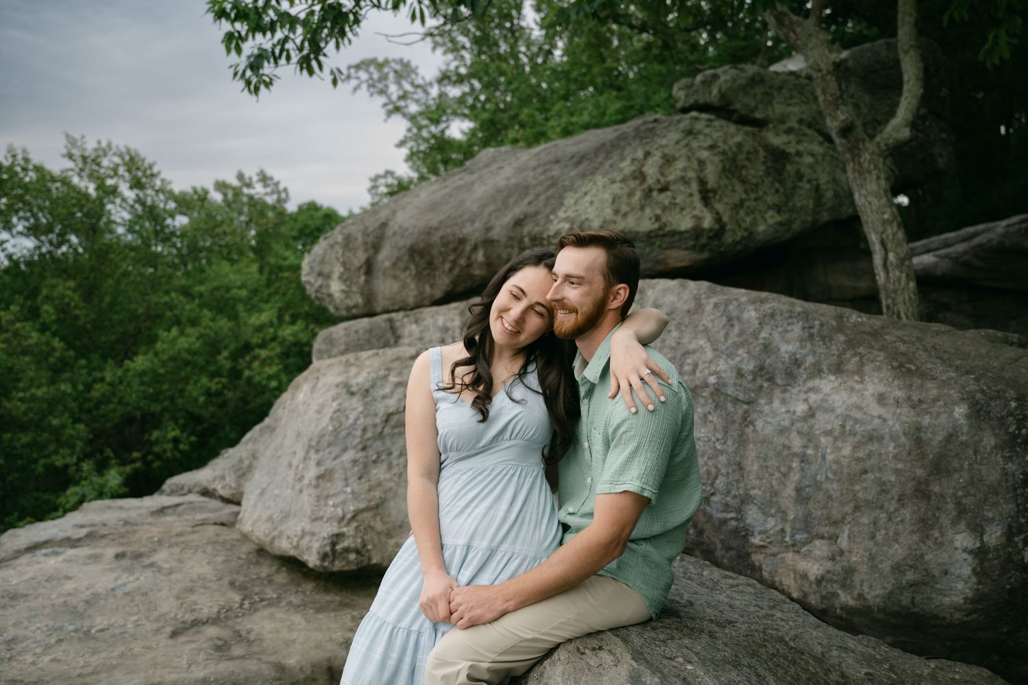 Intimate moment captured on rocky terrain with forest backdrop and overcast sky.