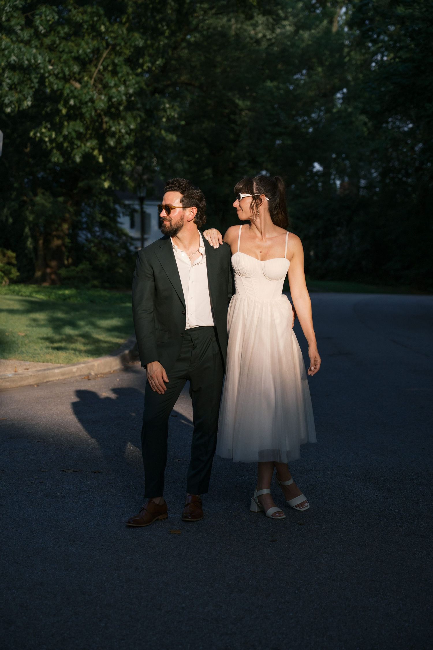 A bride and groom walk together at dusk along a darkening outdoor path.