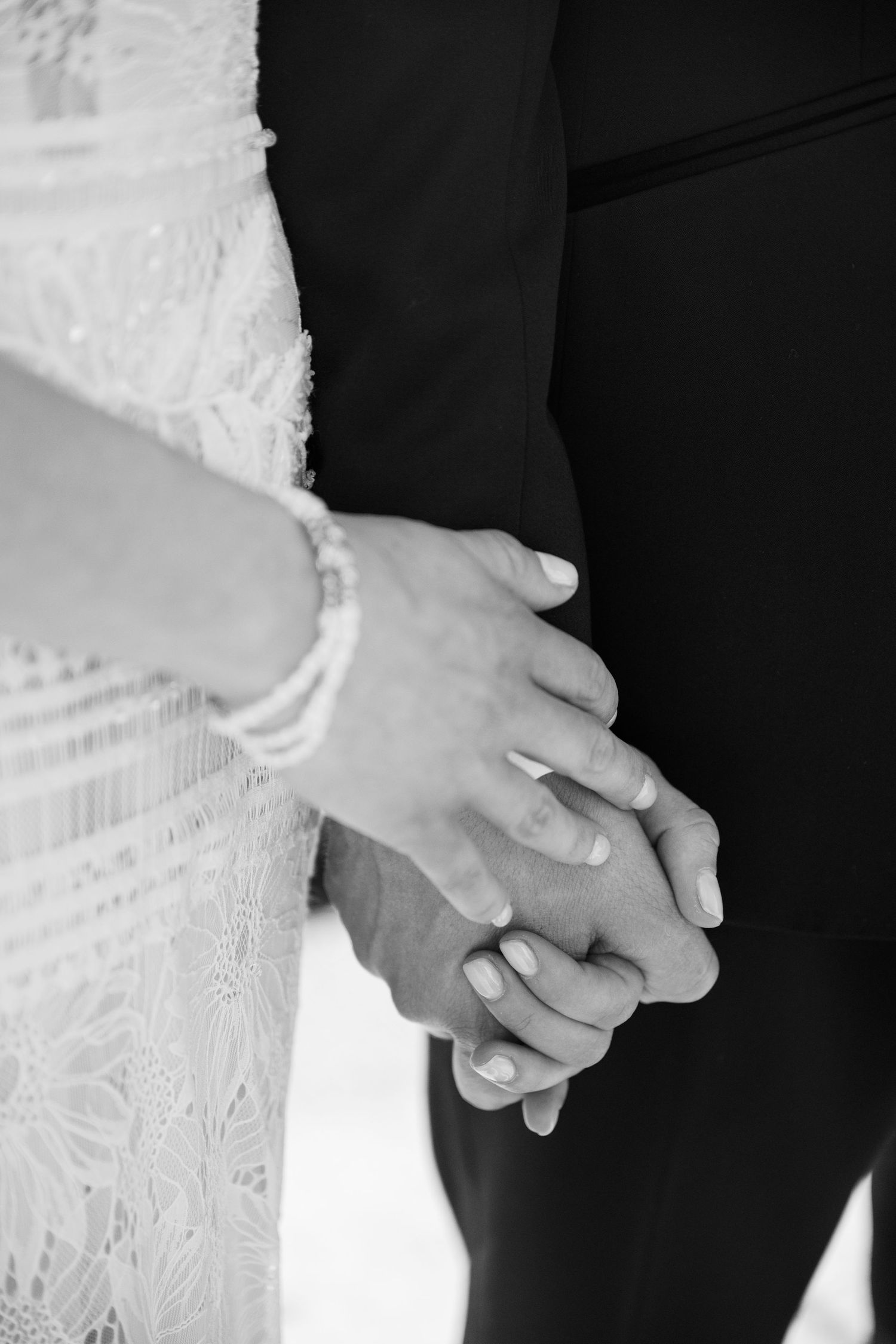 Close-up black and white photo of clasped hands wearing wedding rings.