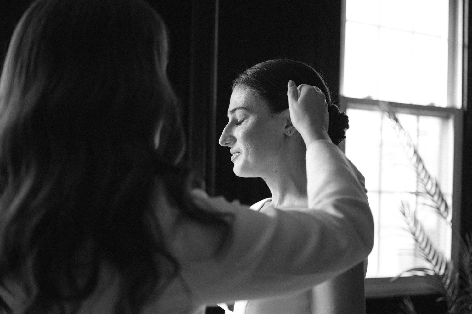 A silhouetted person looks through a window while smoking a cigarette, creating a moody black and white portrait.