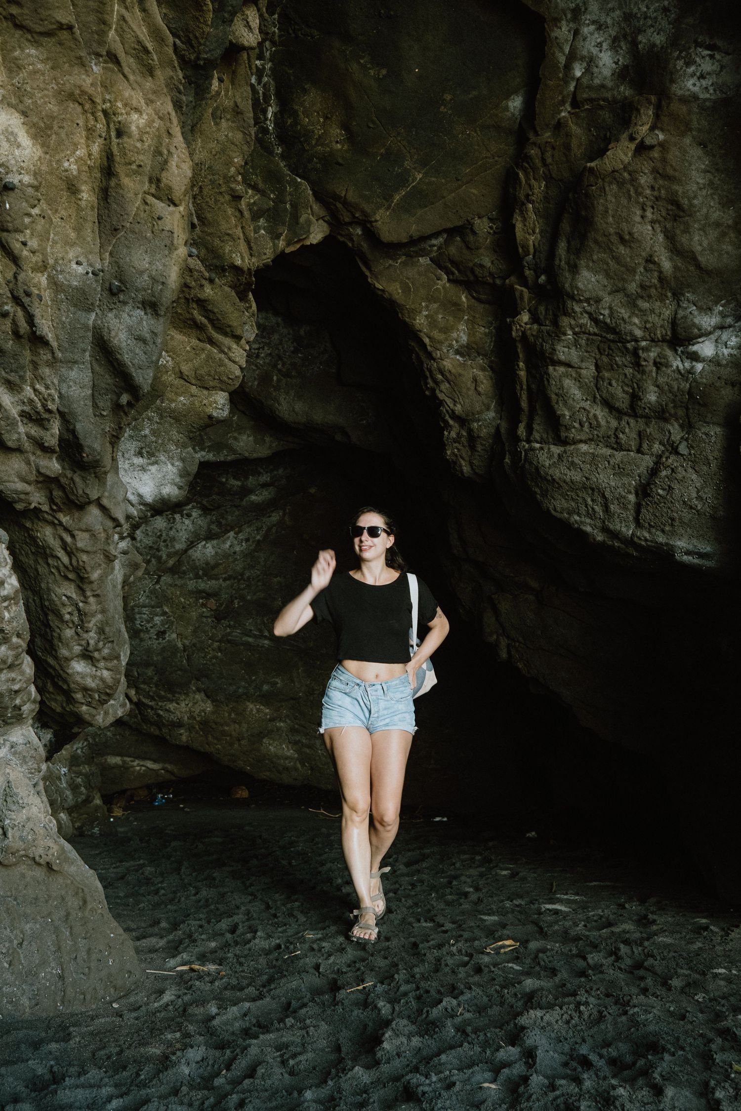 Figure exploring a dark rocky cave entrance near the beach.