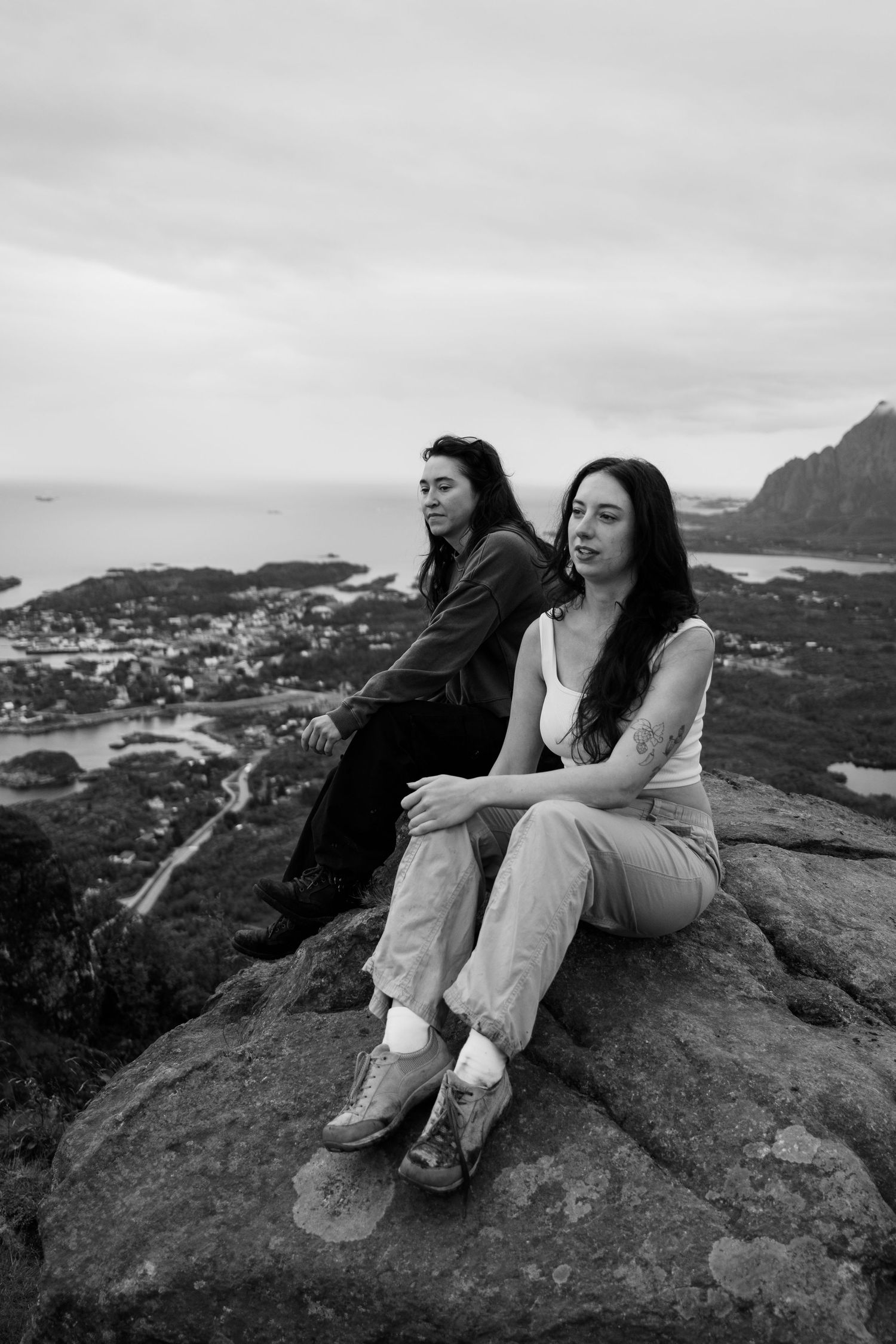 Two people sitting on a rocky overlook with dramatic coastal views in black and white.