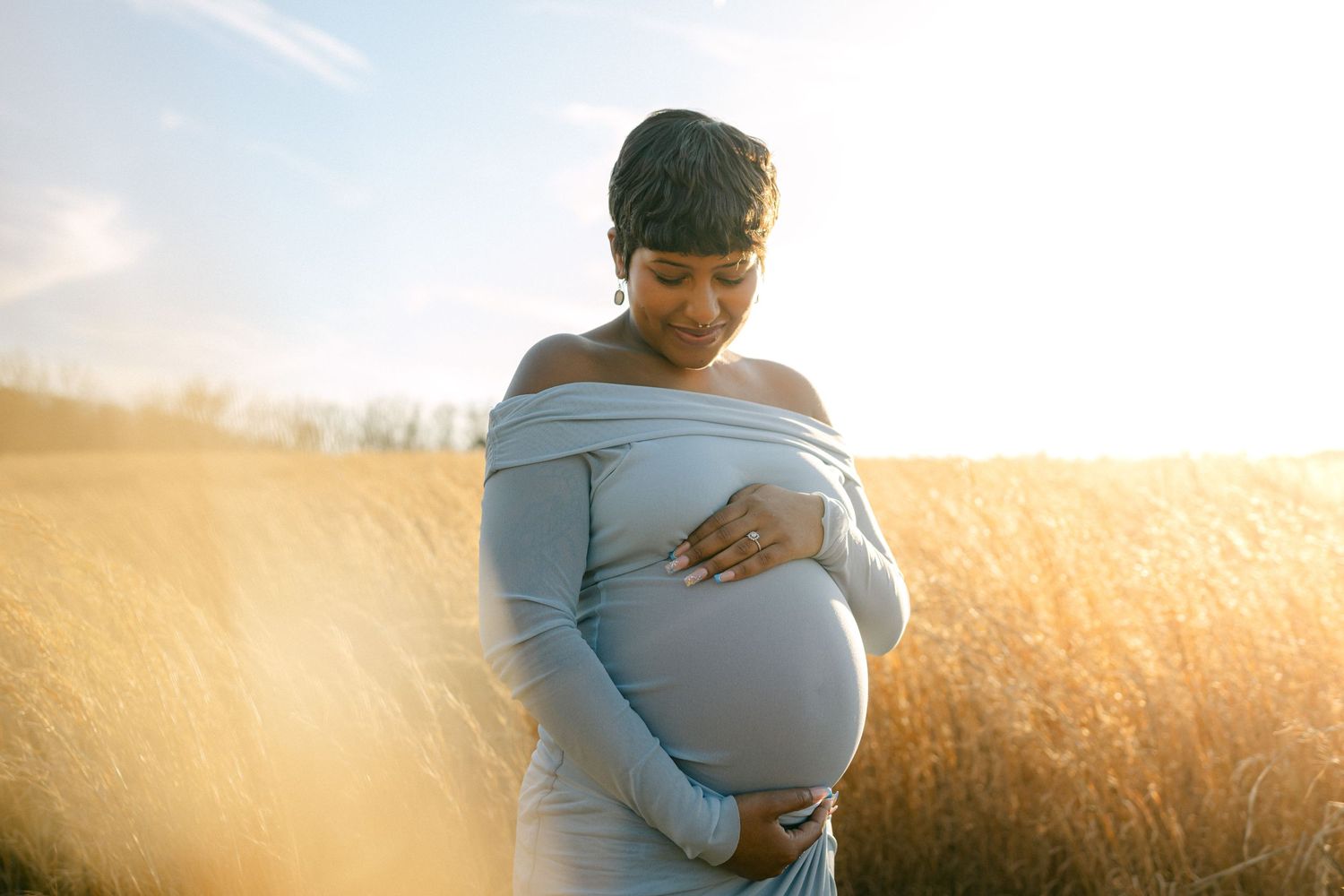close up maternity photo of woman holding baby bump in field