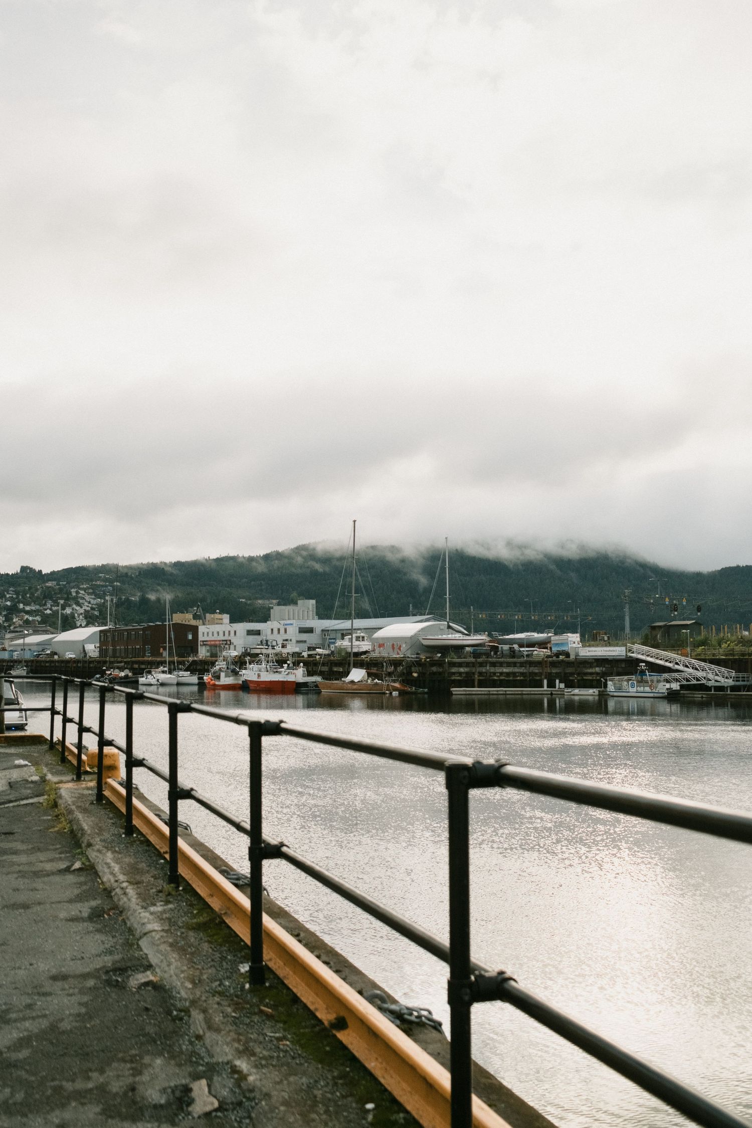 Misty harbor with boats and mountains visible through foggy conditions.
