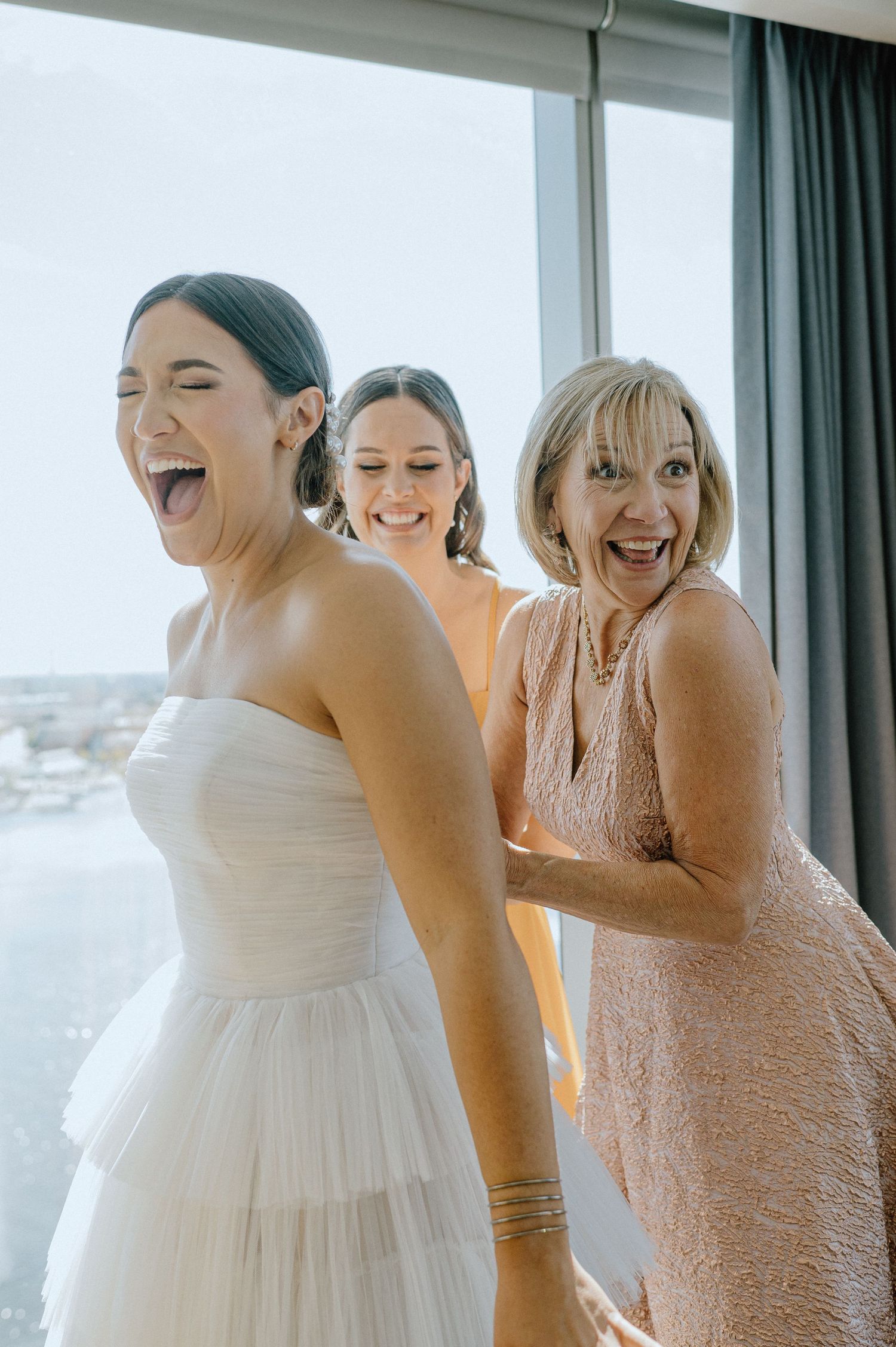 Joyful moment shared between women during wedding preparations by a window.