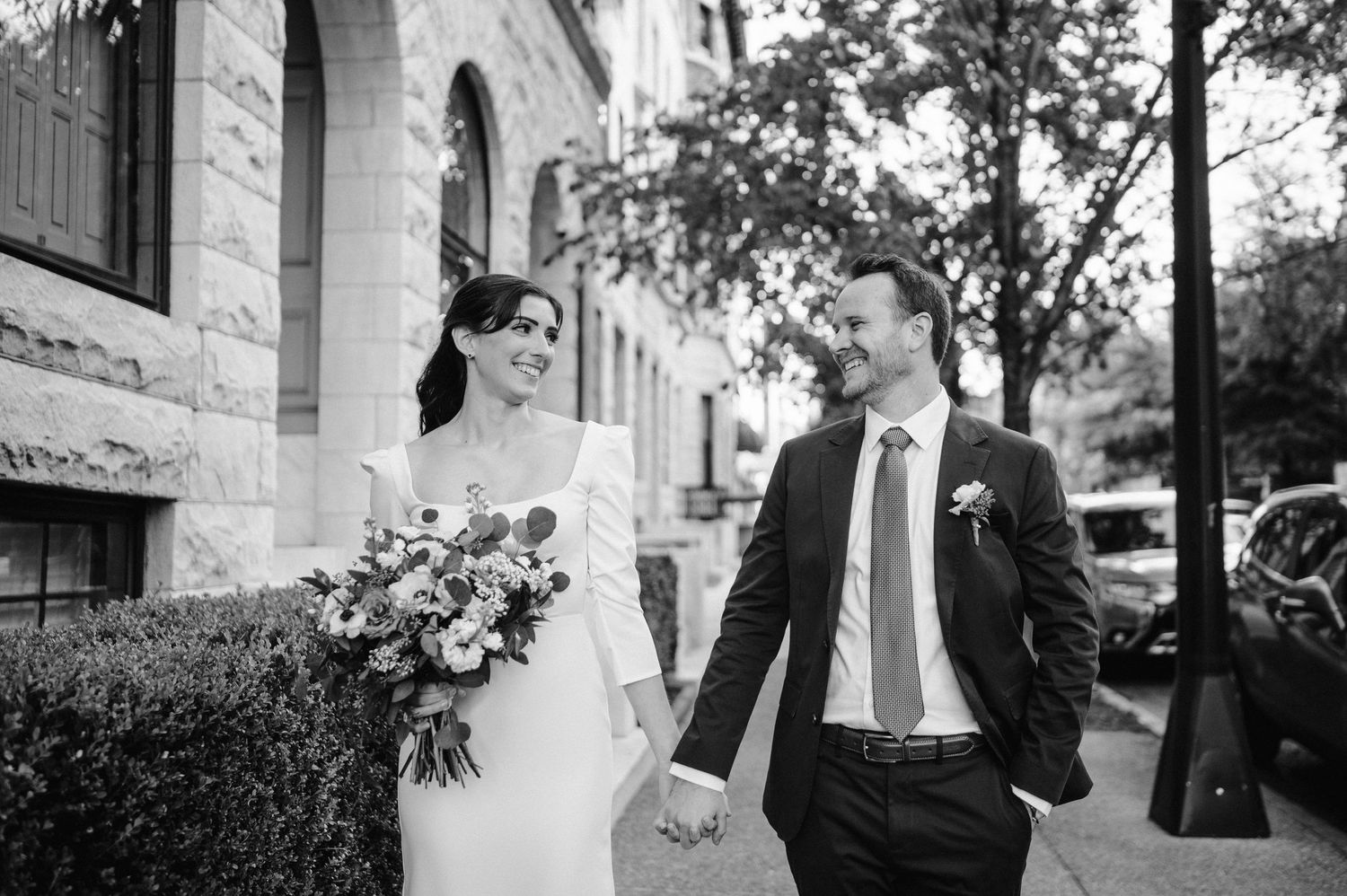 Bride holding colorful bouquet walks with groom outside historic stone building.