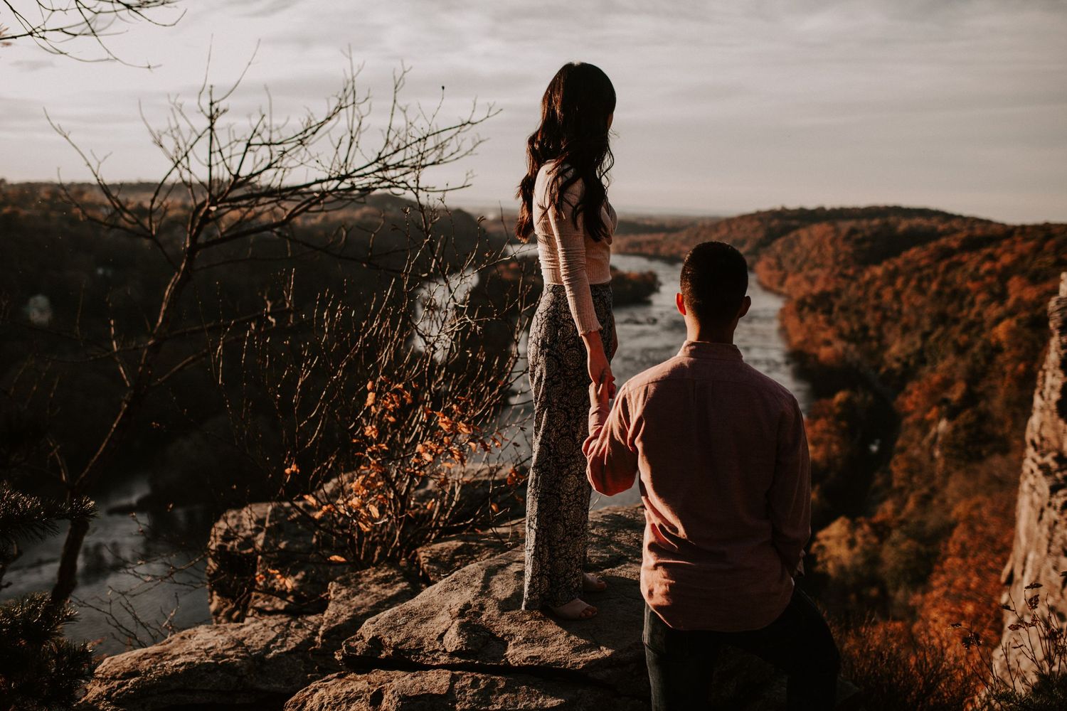 Silhouetted figures stand on rocky outcrop overlooking autumn valley landscape.
