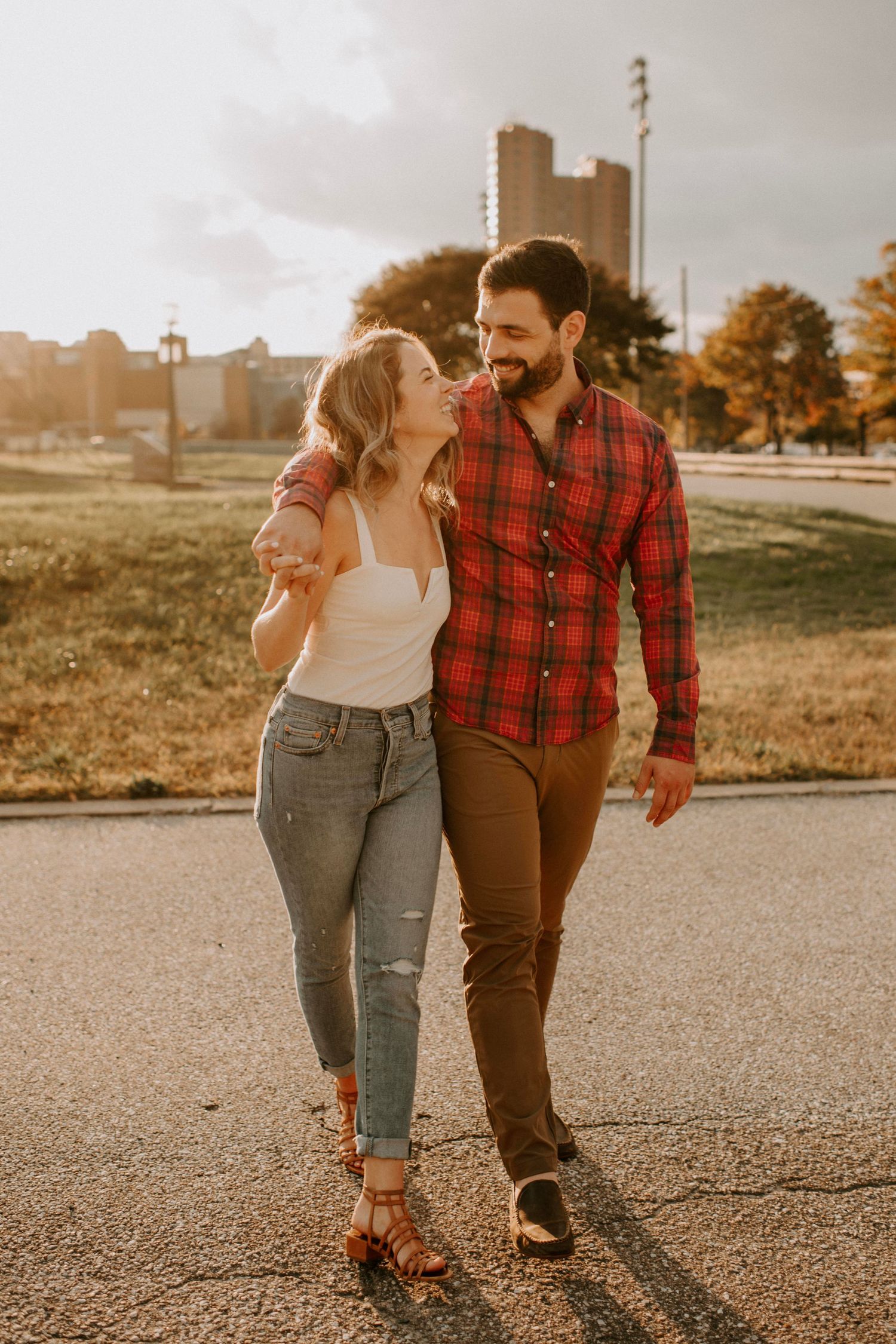 Couple walking together at sunset in casual attire with urban background.