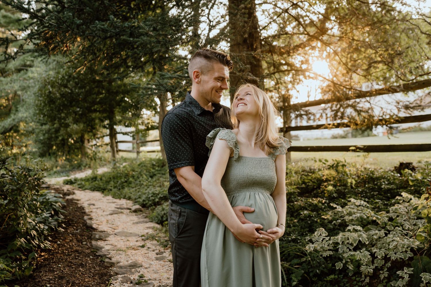 Couple embracing on garden path with golden sunset light filtering through trees.