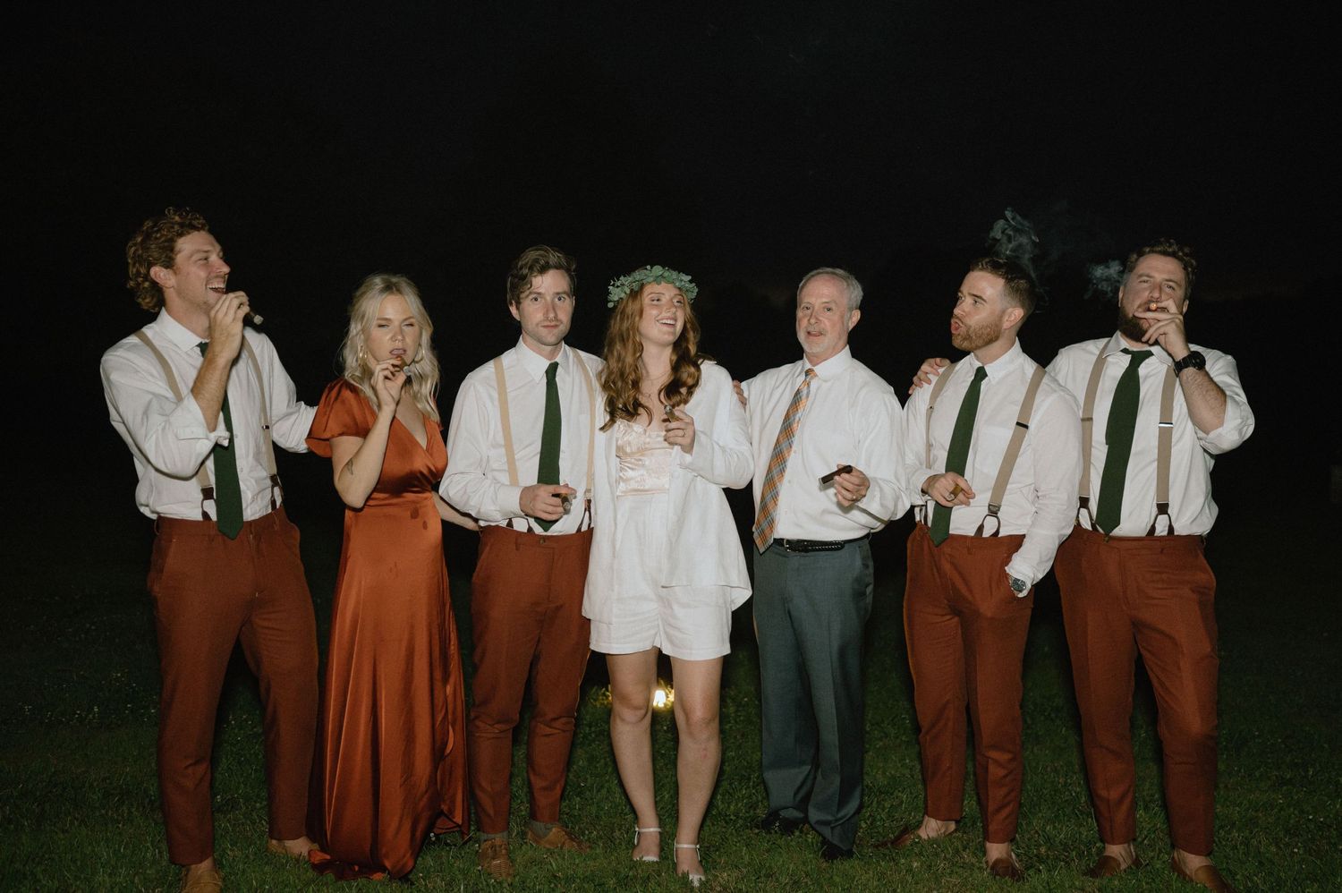 Wedding party in burgundy and white attire posing together at night.