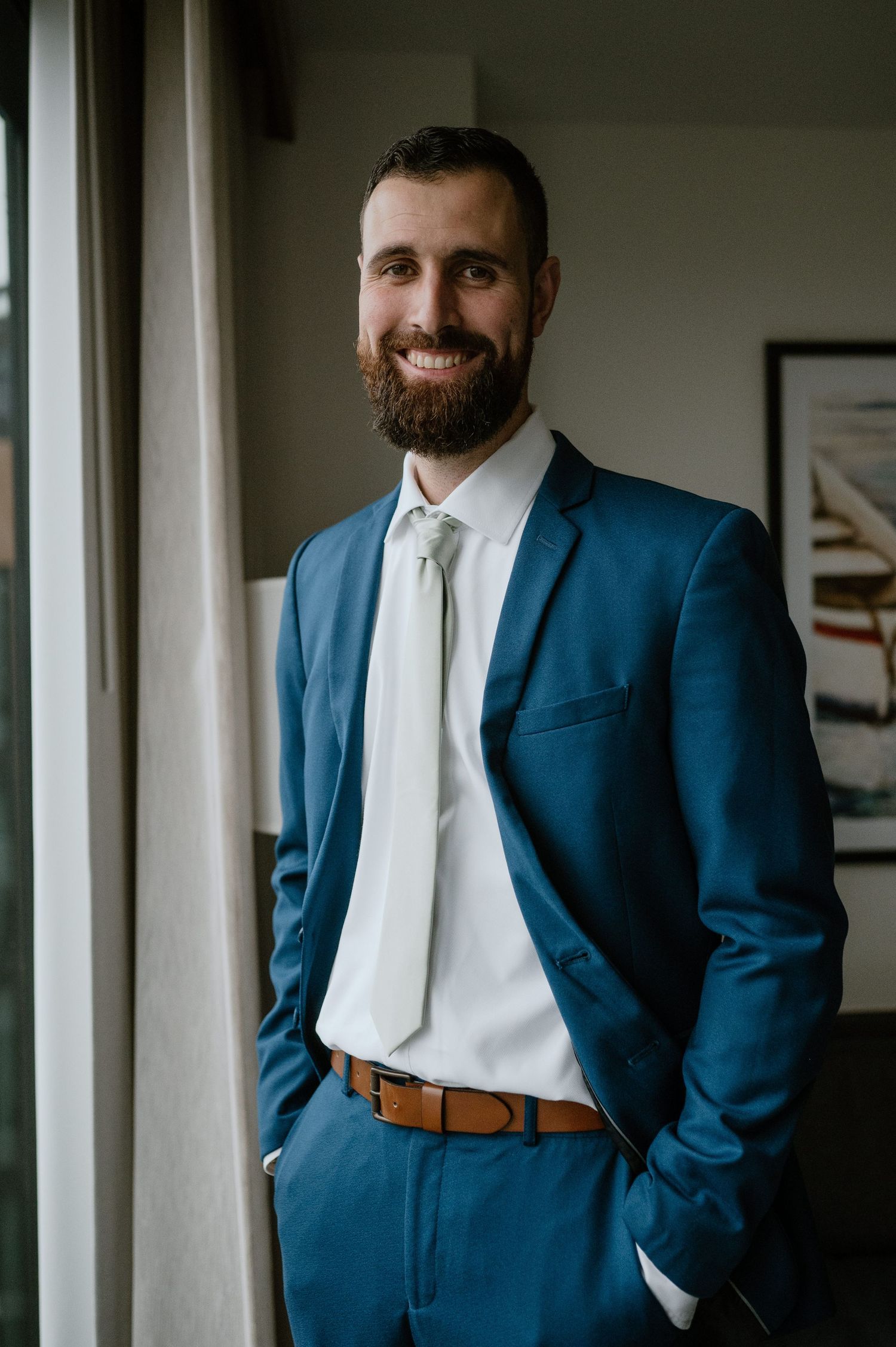 Person in blue suit and white tie poses near window in modern interior.