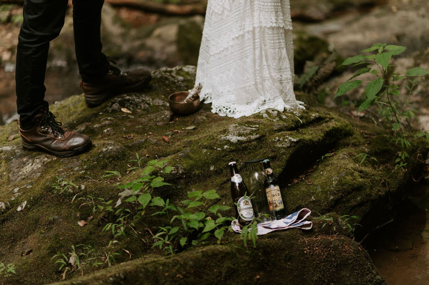 Wedding ceremony items and supplies arranged on mossy rocks in a forest setting.