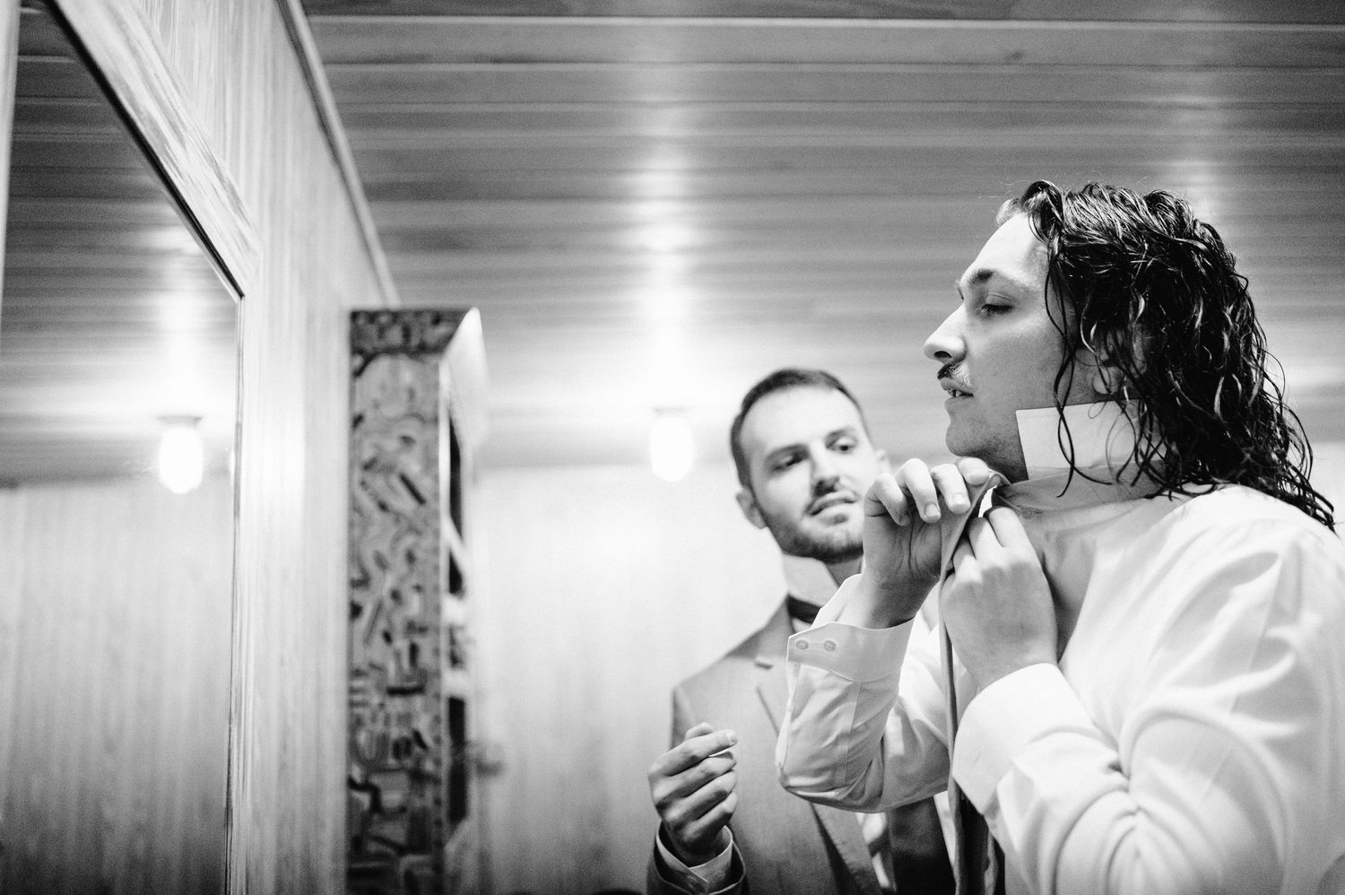 Two men in casual attire share a candid black and white moment in an indoor setting.