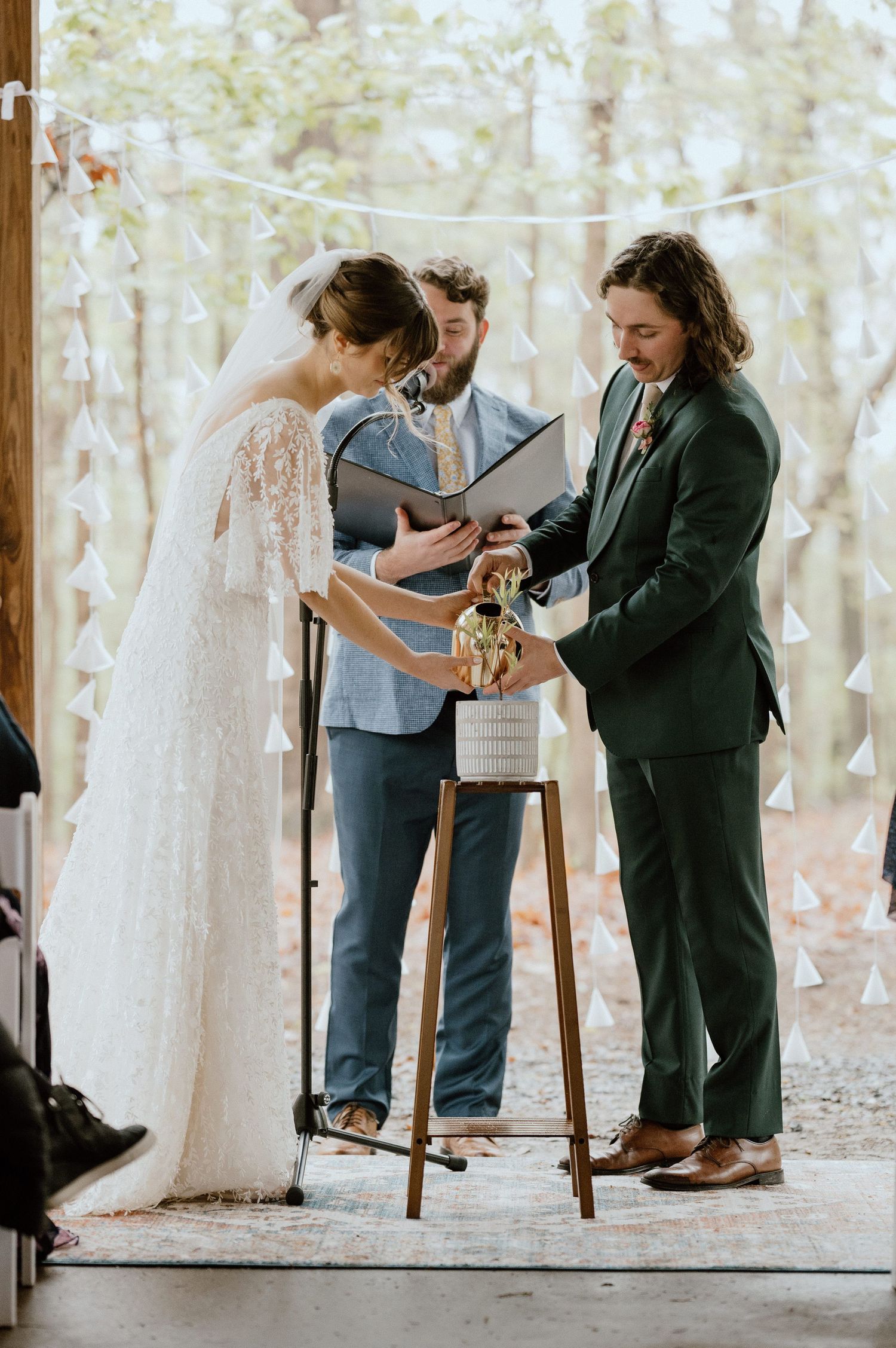 Intimate wedding ceremony moment under decorated wooden pavilion in forest setting.