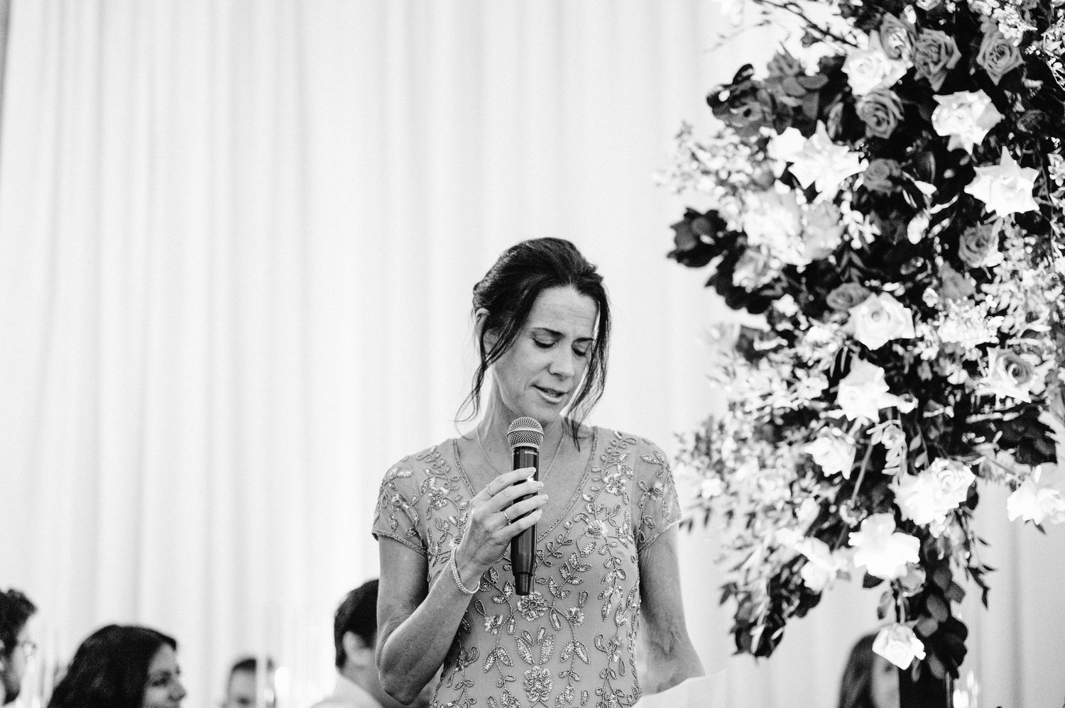 Wedding reception speech moment captured in black and white with floral backdrop.