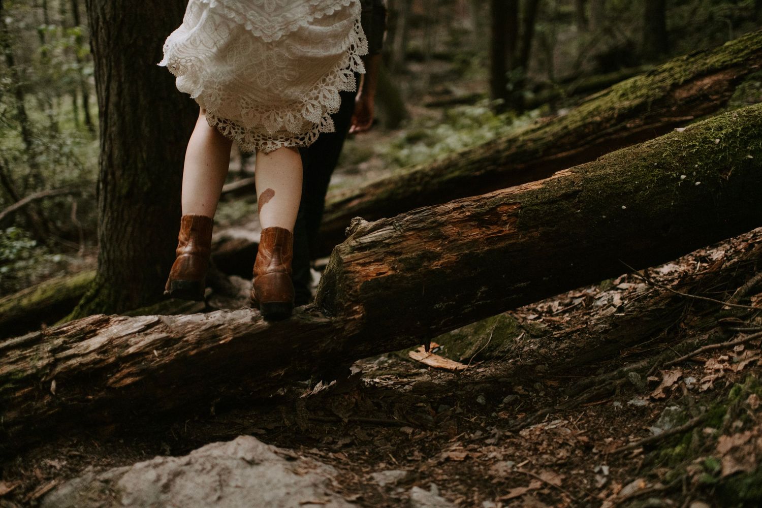 Brown leather boots and white lace dress hem visible on a mossy fallen log.