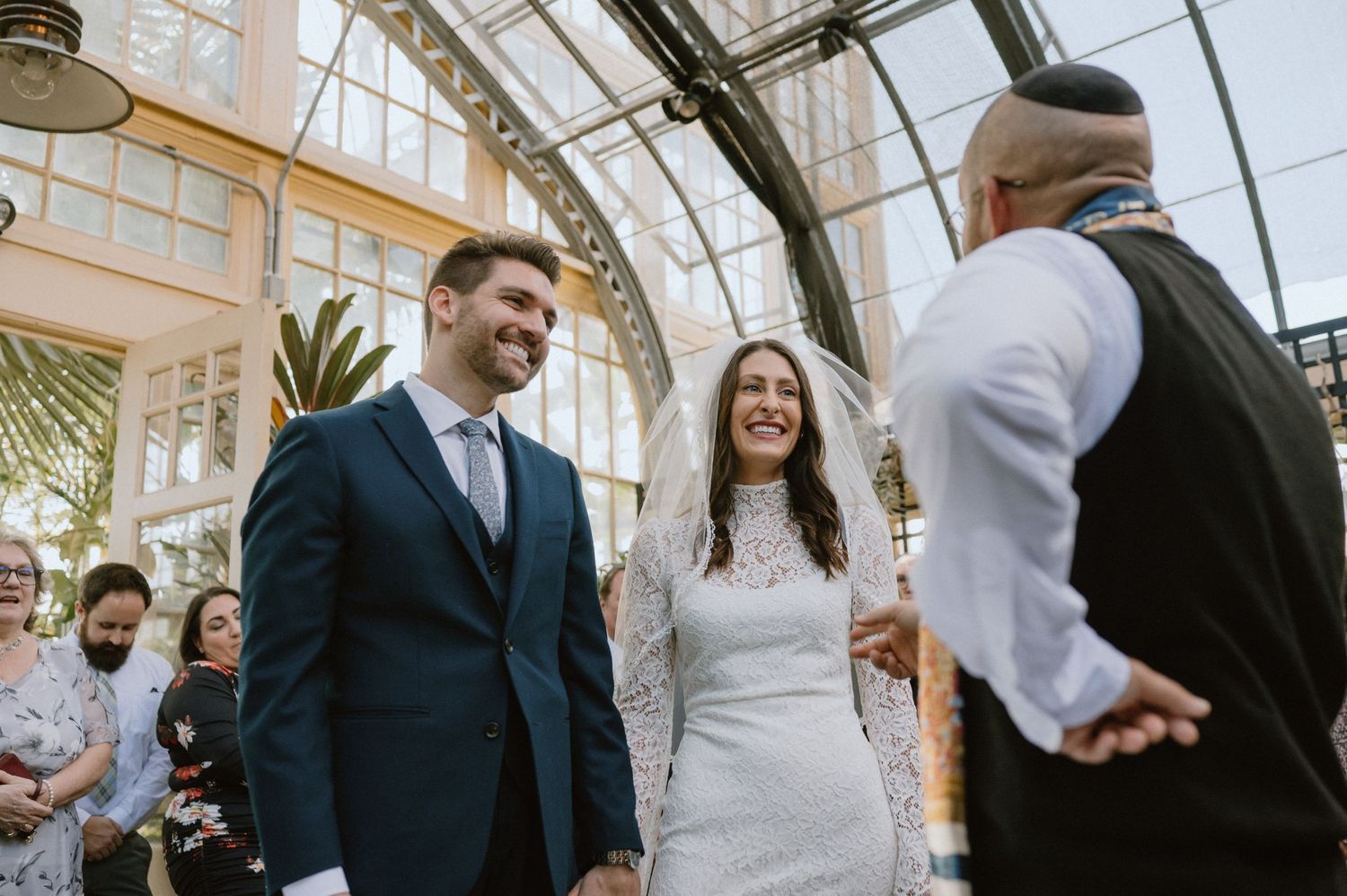 A wedding ceremony taking place in a bright conservatory with glass ceilings and greenery.