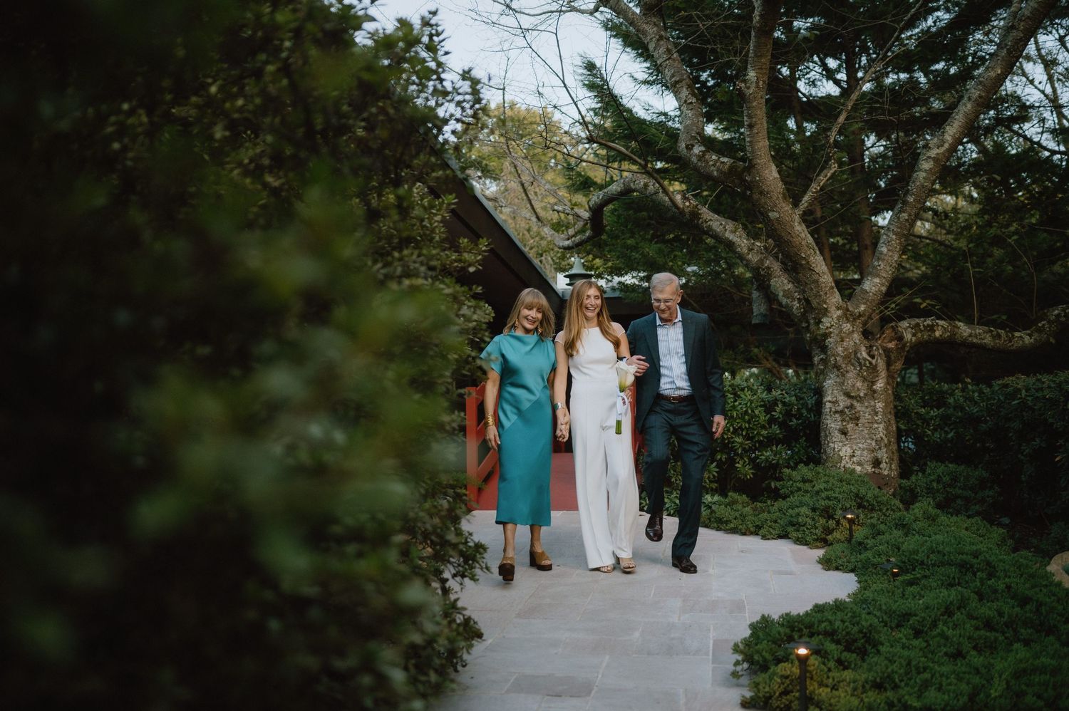 Wedding party members walking along a stone path surrounded by lush greenery.