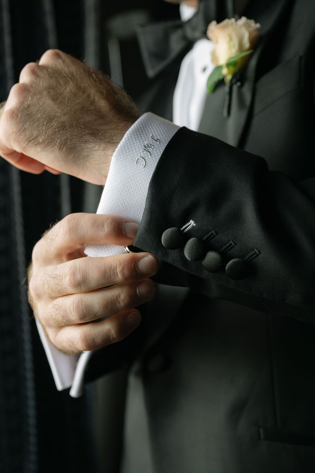 Close-up of hands adjusting white cuffs and cufflinks on formal black tuxedo sleeves.
