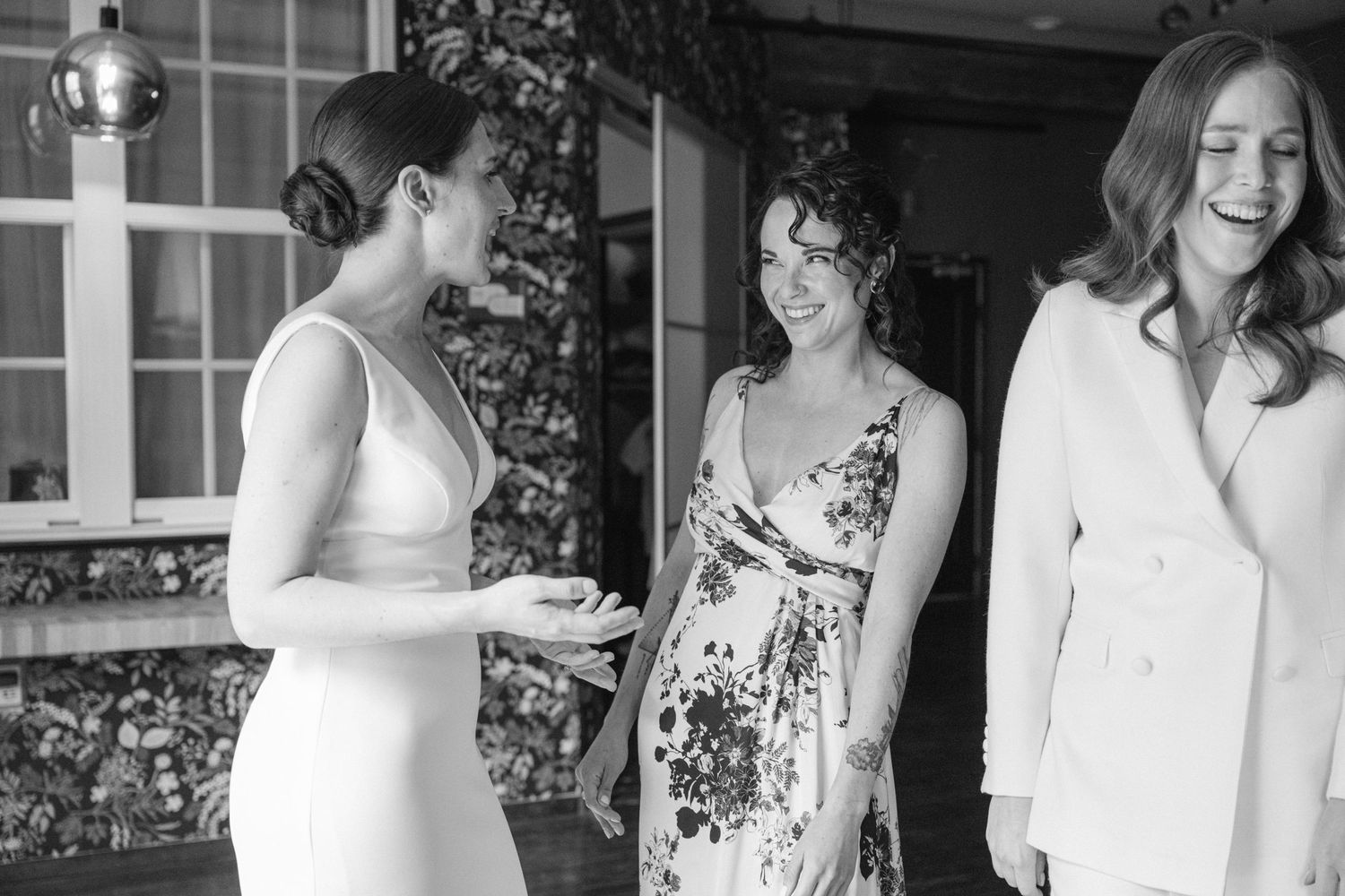 A black and white photo shows three people in formal attire conversing outside a window.