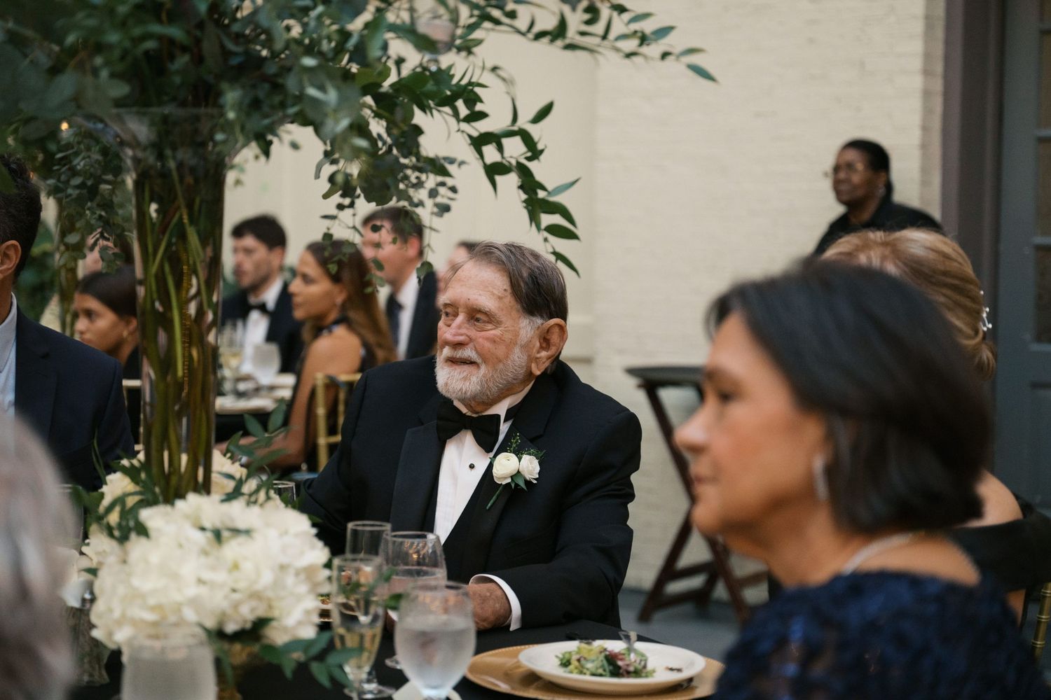 Wedding guests seated at elegant dinner tables with white floral centerpieces.