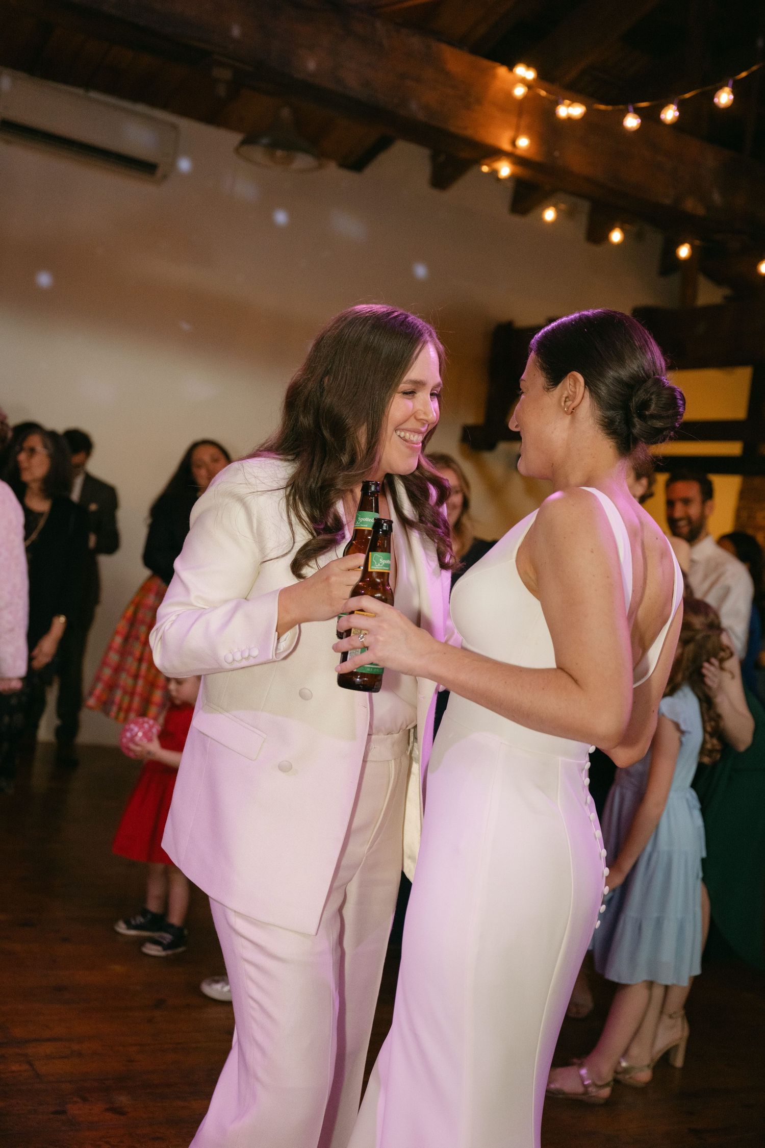 People dance and socialize at what appears to be a wedding reception under warm string lights.