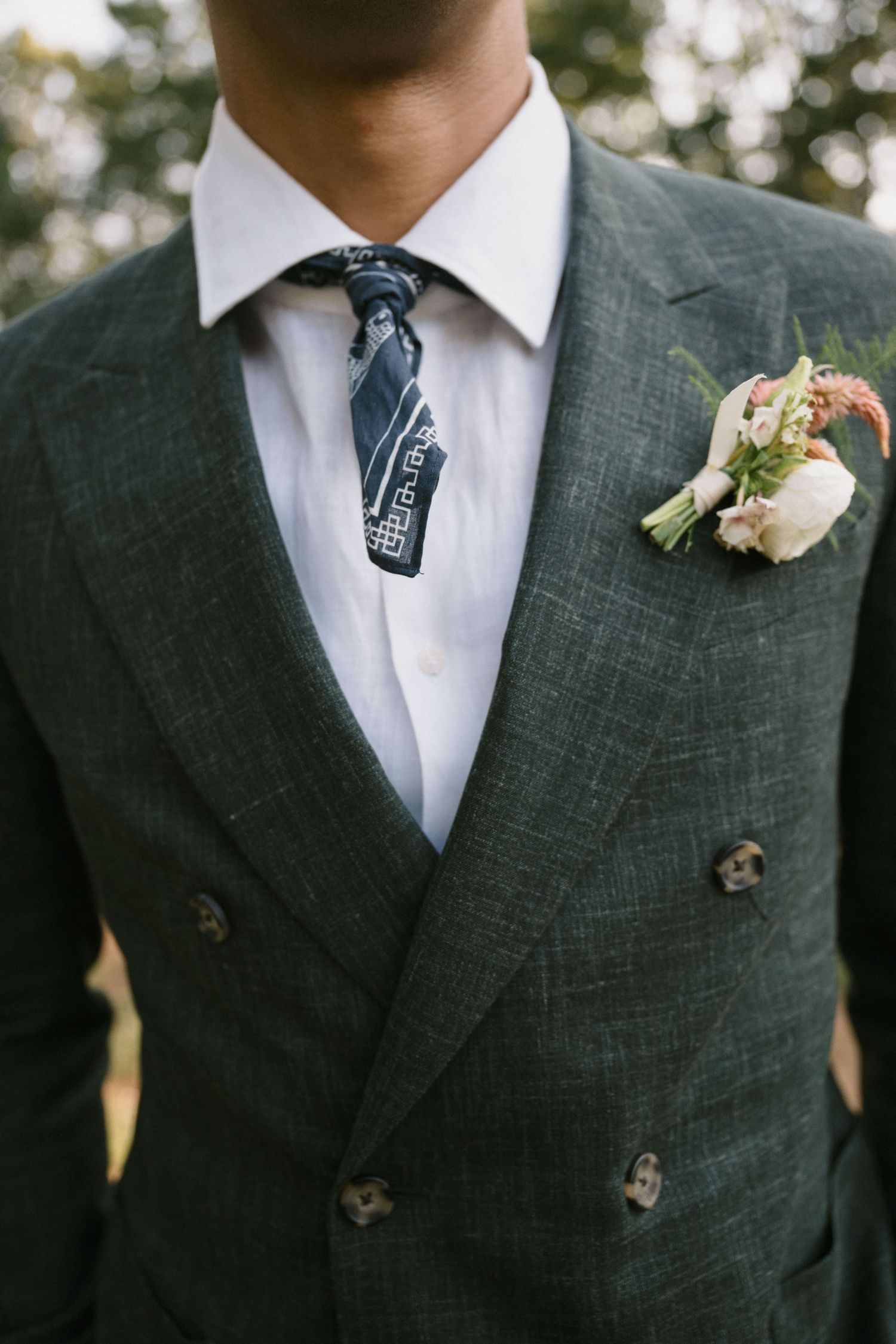 Close-up detail of a groom's dark double-breasted suit with floral boutonniere and patterned tie.
