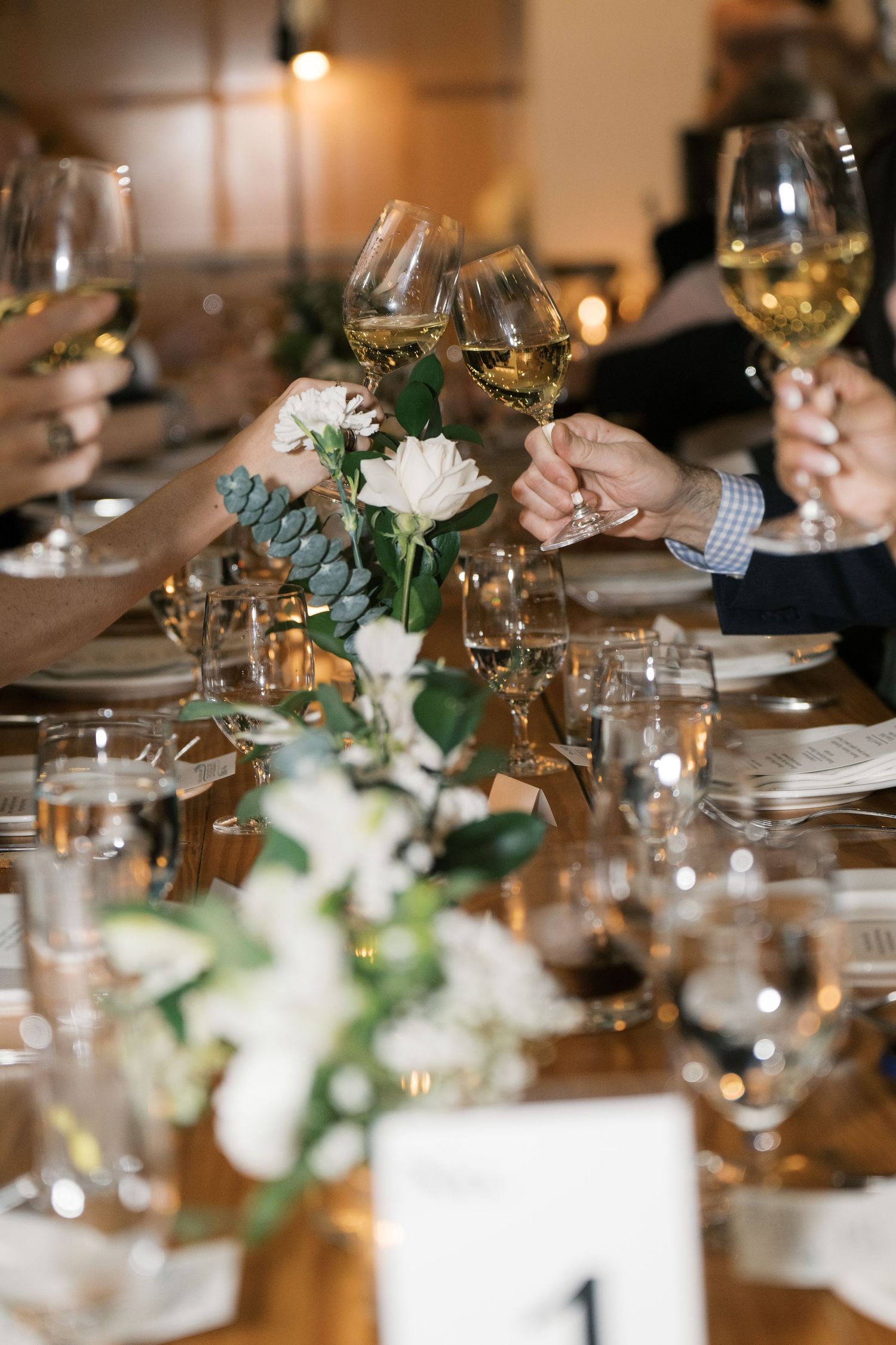 Elegant table setting with wine glasses, white floral centerpieces and greenery at a wedding reception.