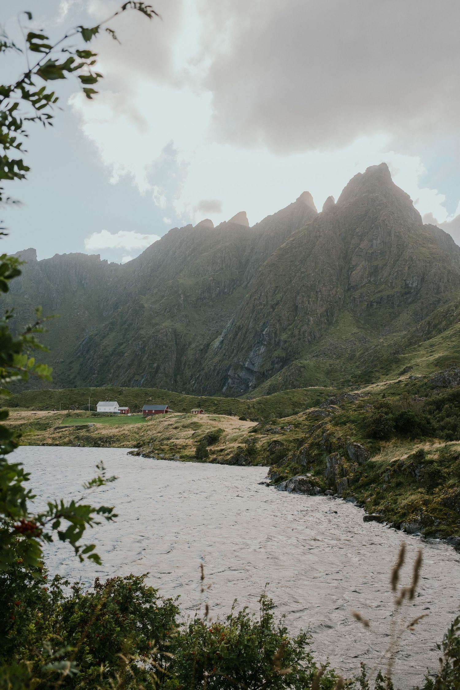 Dramatic mountain peaks rise above a lake with a small white building visible on the shore.