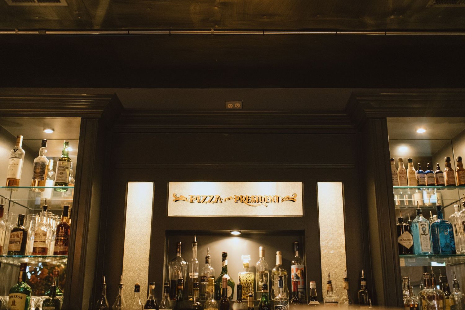 Bar interior with illuminated bottles and glassware on display shelves.