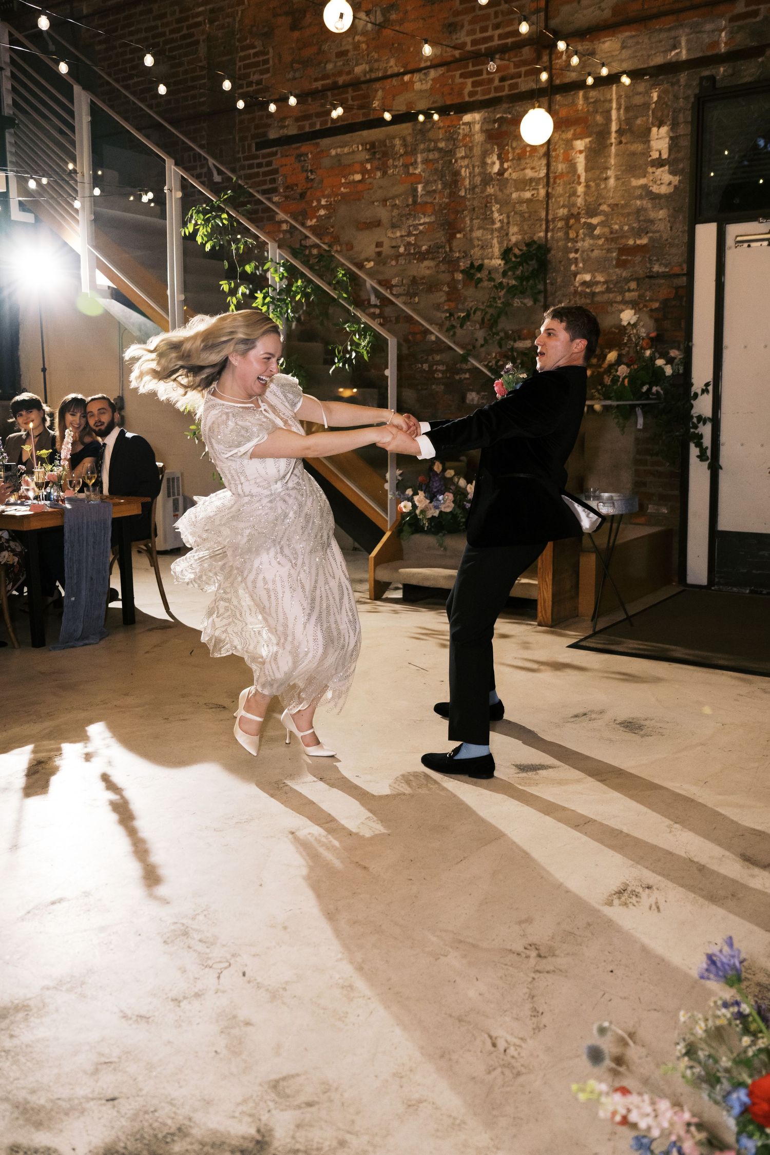 Dancing couple at wedding reception with bride's dress twirling in an industrial-style venue.