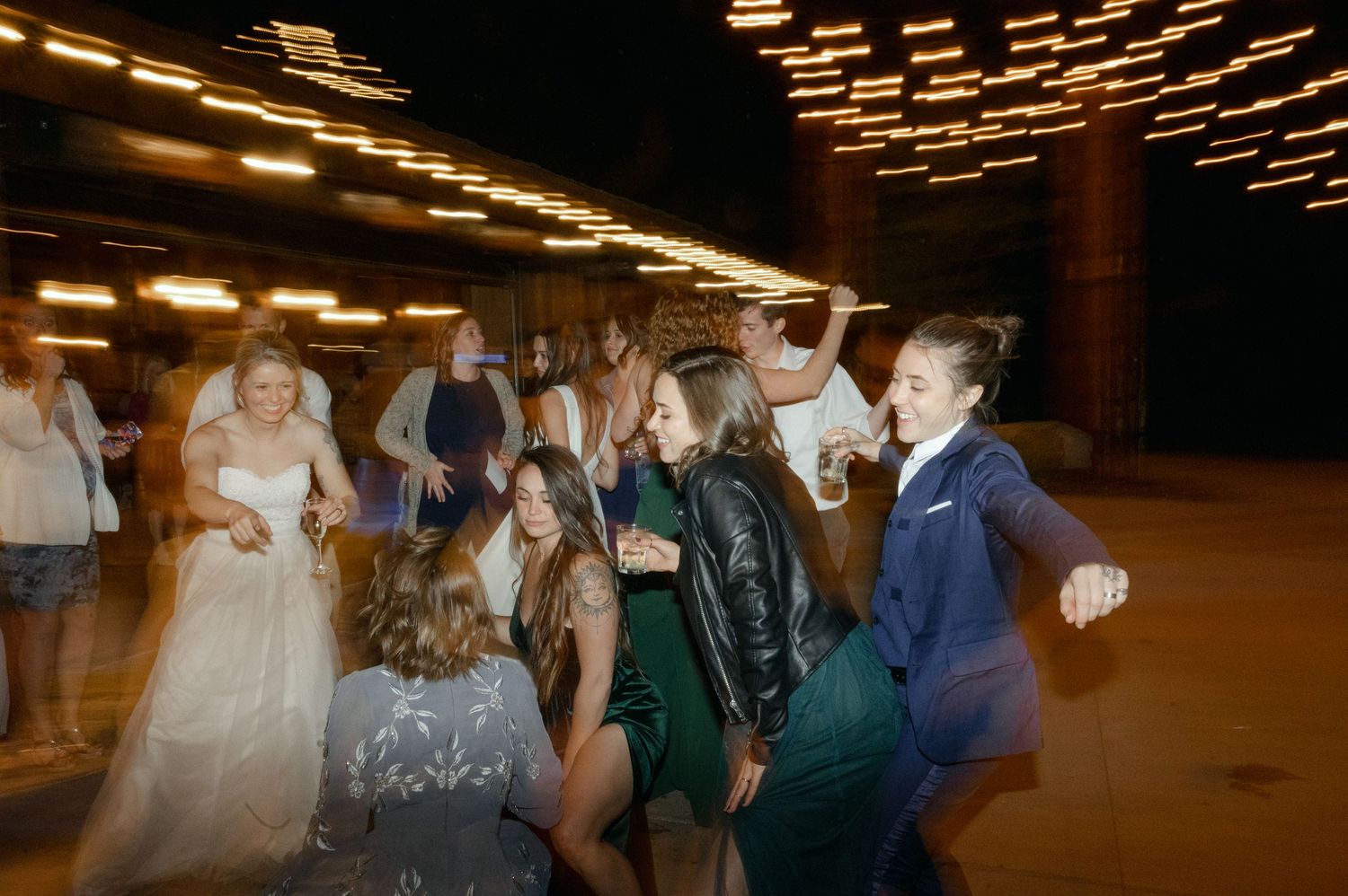Wedding reception dance floor with guests dancing under geometric ceiling lights creating a motion blur effect.