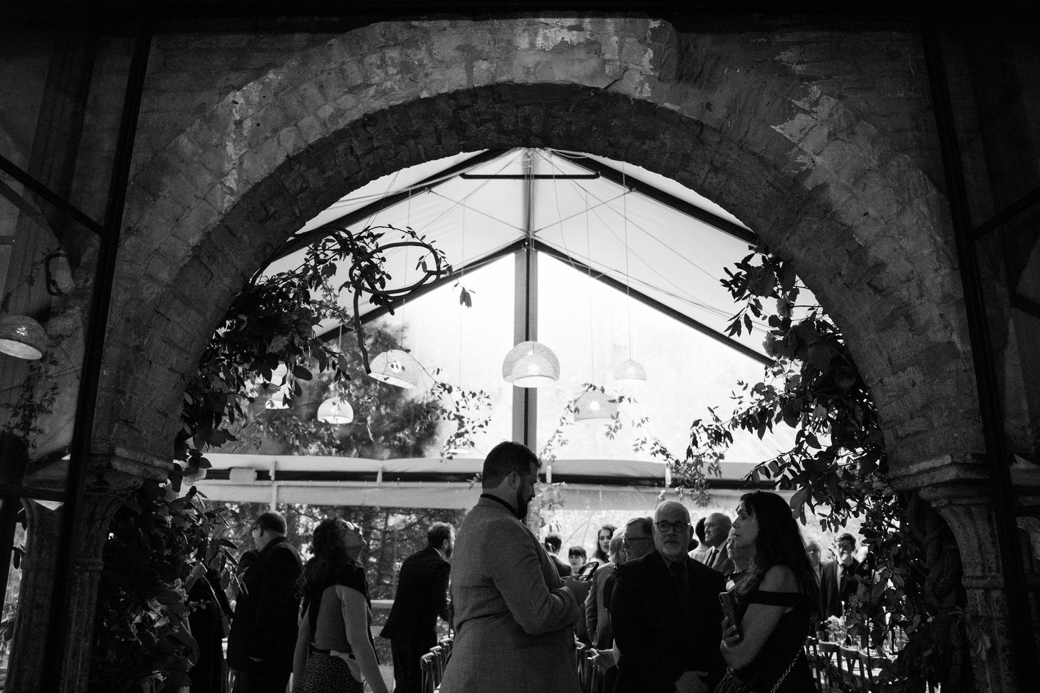 Wedding guests gather under an arched doorway with a church steeple visible in the background.