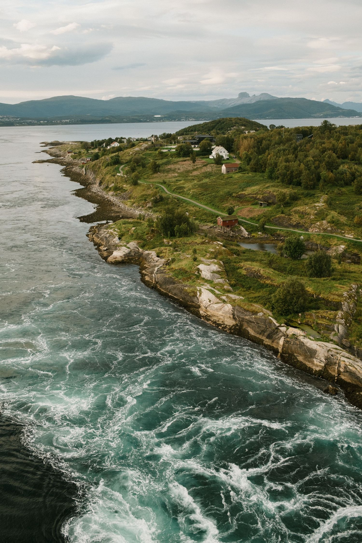 Aerial view of rugged coastline with waves crashing against rocky cliffs and scattered houses.