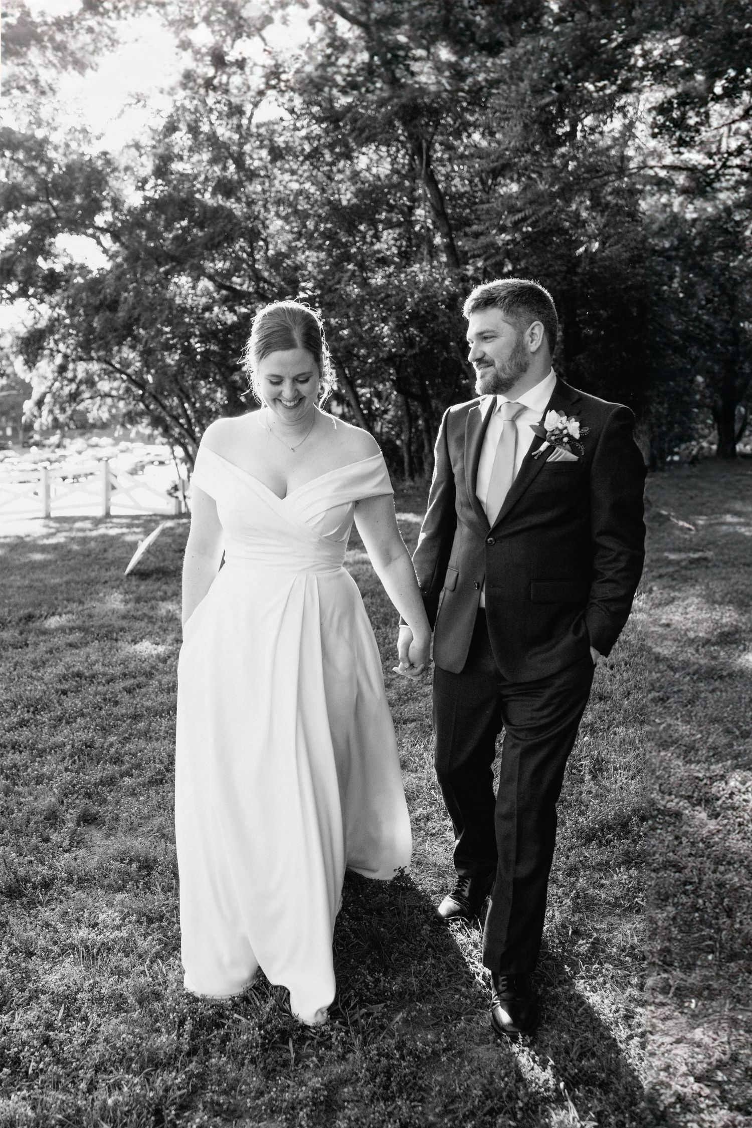 A couple walks hand in hand on grass during their wedding day.