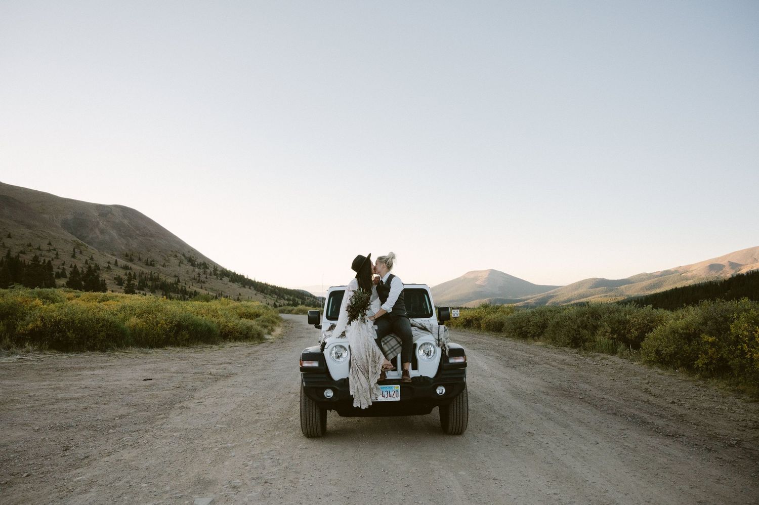 A couple sits on their white Jeep during a mountain adventure session.