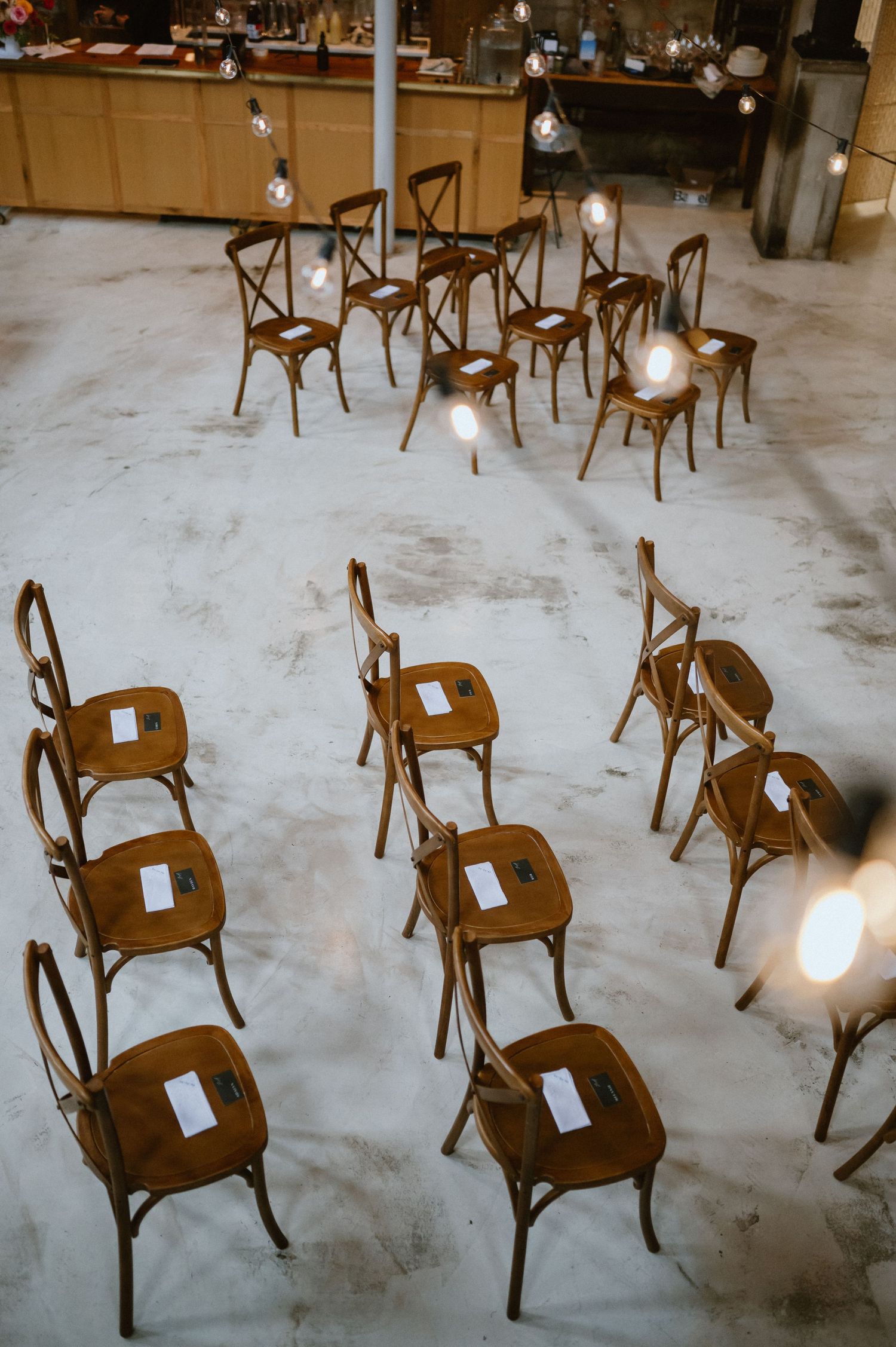 Wooden crossback chairs arranged in rows with paper programs for a wedding ceremony.