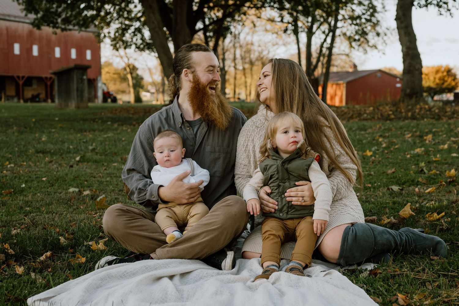 A family group portrait taken outdoors on a white blanket during fall.